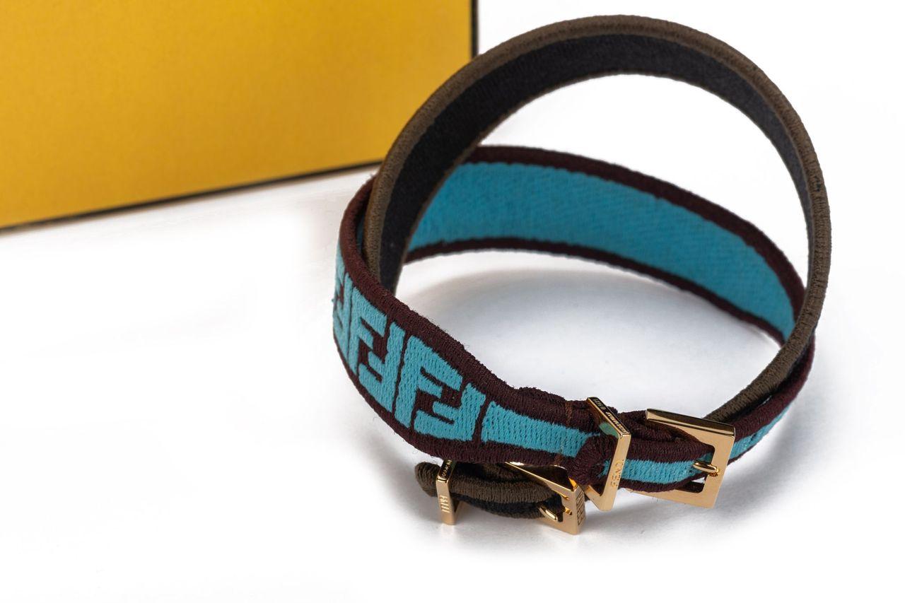 Set de 2 bracelets monogramme Fendi en tissu turquoise et marron. La quincaillerie est dorée et se compose d'un fermoir de chaque côté. La pièce est neuve et est accompagnée d'une boîte et d'une étiquette.