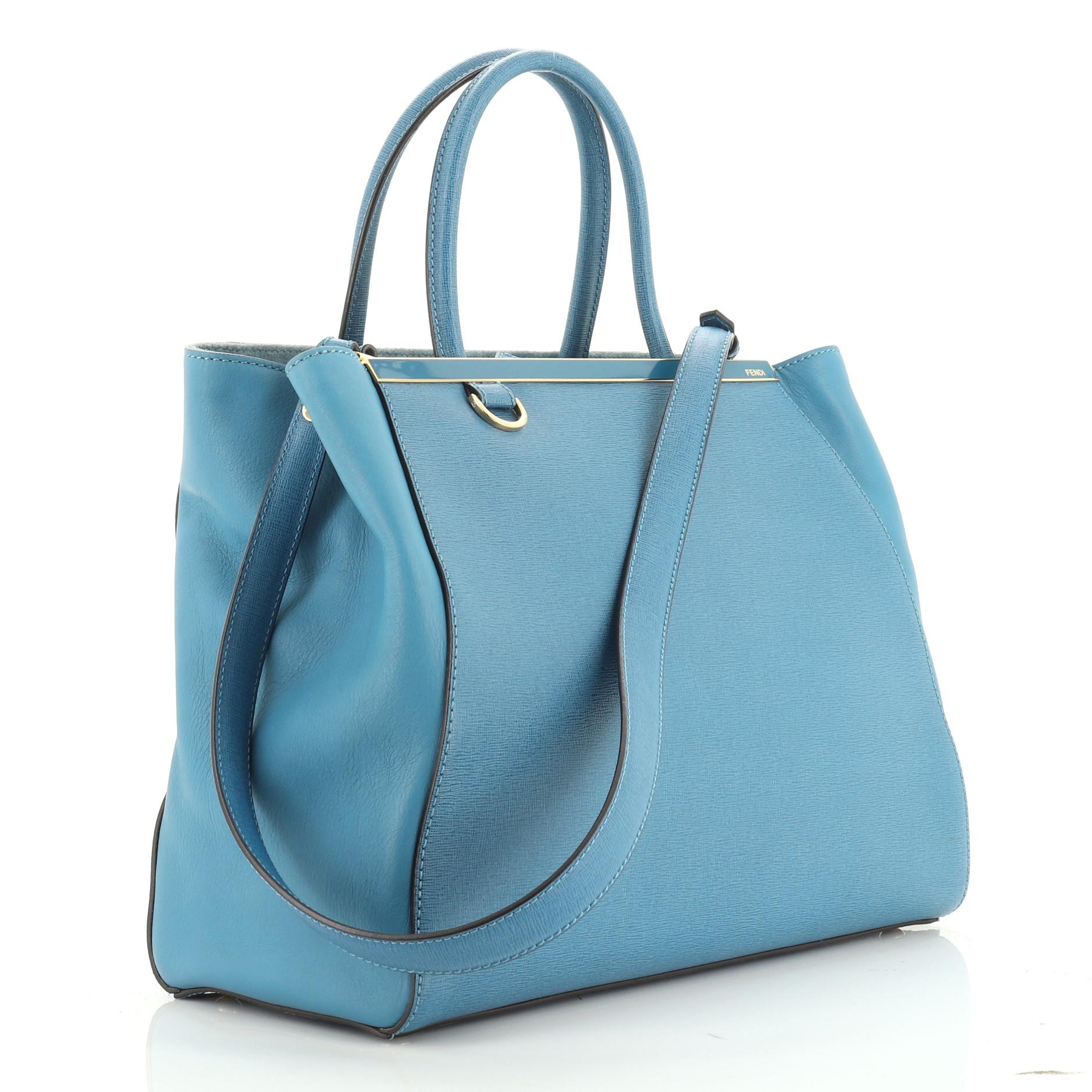 This Fendi 2Jours Bag Leather Medium, crafted from blue leather, features dual rolled leather handles, top bar with Fendi brand name, and gold-tone hardware. Its top snap tab closure opens to a blue fabric interior with a middle zip compartment and