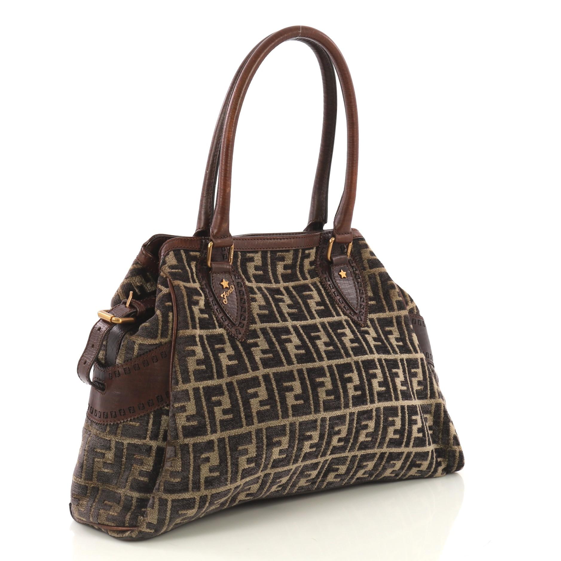 This Fendi Bag Du Jour Zucca Velvet Medium, crafted in brown zucca velvet, features dual-rolled leather handles, exterior side pockets, and gold-tone hardware. Its press stud closures opens to a brown zucca velvet interior with zip pocket.