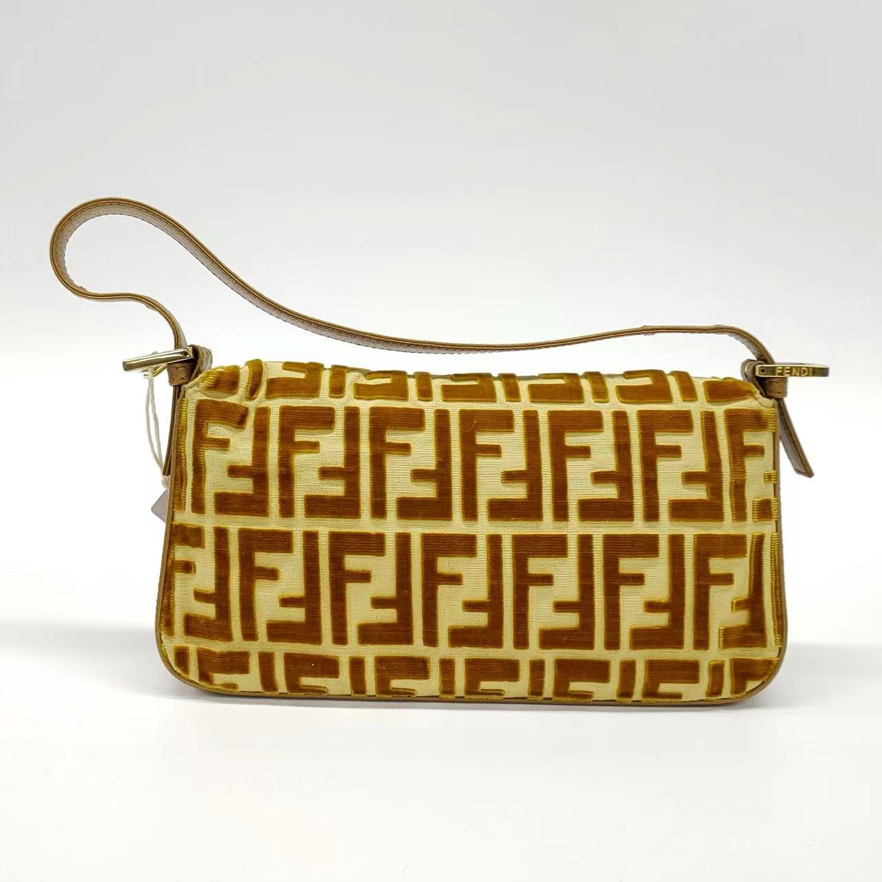 FENDI Baguette Gold FF Monogram Velvet Shoulder Bag

  This FENDI Baguette is a stunning piece, featuring FF monogram embroidery on gold velvet. This design makes for a bold and eye-catching accessory. 
  CONDITION: EXCELLENT
  DETAILS:
  
  Model: