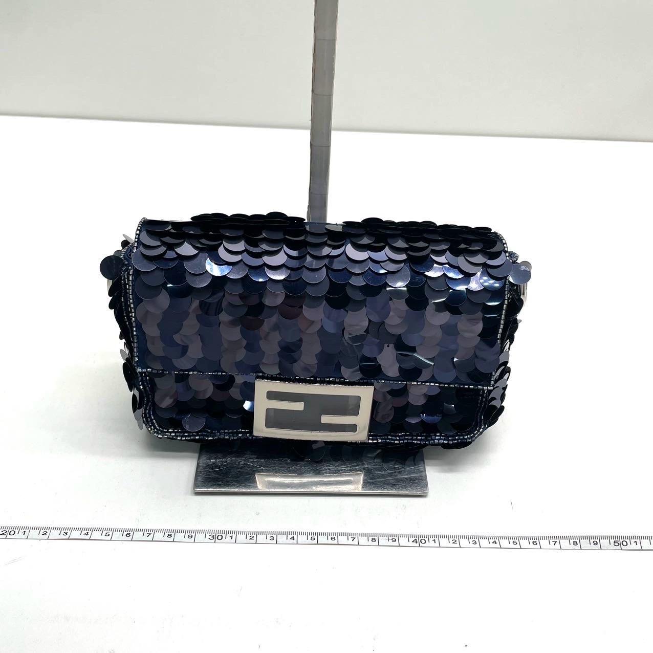 Faites l'expérience du luxe et du style avec le mini sac à bandoulière Baguette de Fendi, orné de paillettes vertes fluo et complété par une bandoulière en chaîne de couleur argentée. Ce mini-sac offre à la fois fonctionnalité et mode. Il peut être