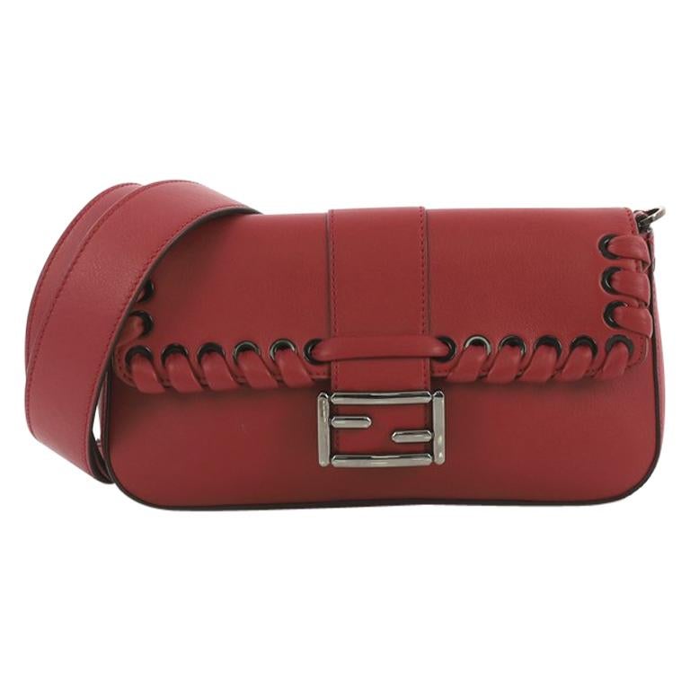 This Fendi Baguette Whipstitch Leather, crafted from red leather, features removable guitar strap, leather whipstitch trim, front flap with Fendi buckle logo and gunmetal-tone hardware. Its snap closure opens to a gray fabric interior with zip