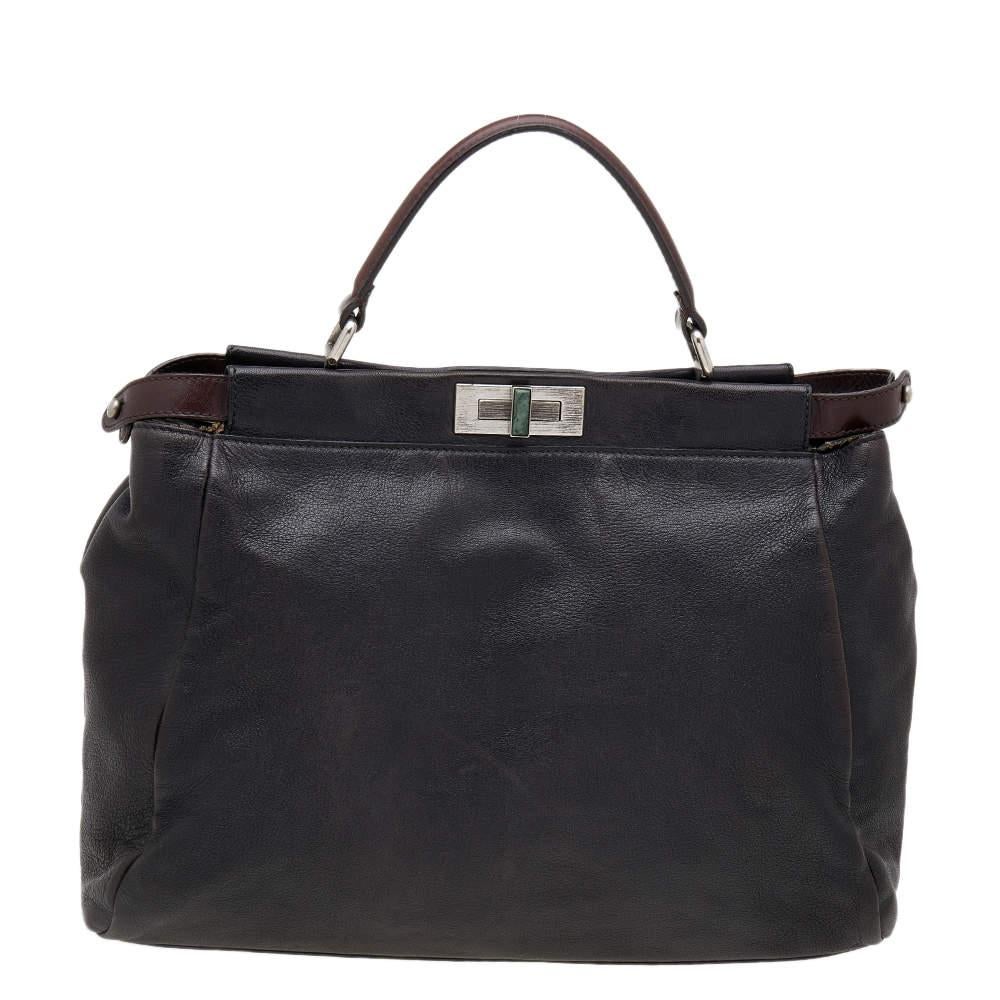 Questa borsa Peekaboo della Maison Fendi è eterna, molto ambita e colpisce tutti per la sua forma, il suo design e la sua bellezza. Questa versione è meticolosamente realizzata in pelle nera e marrone scuro, con un lucchetto argentato con logo