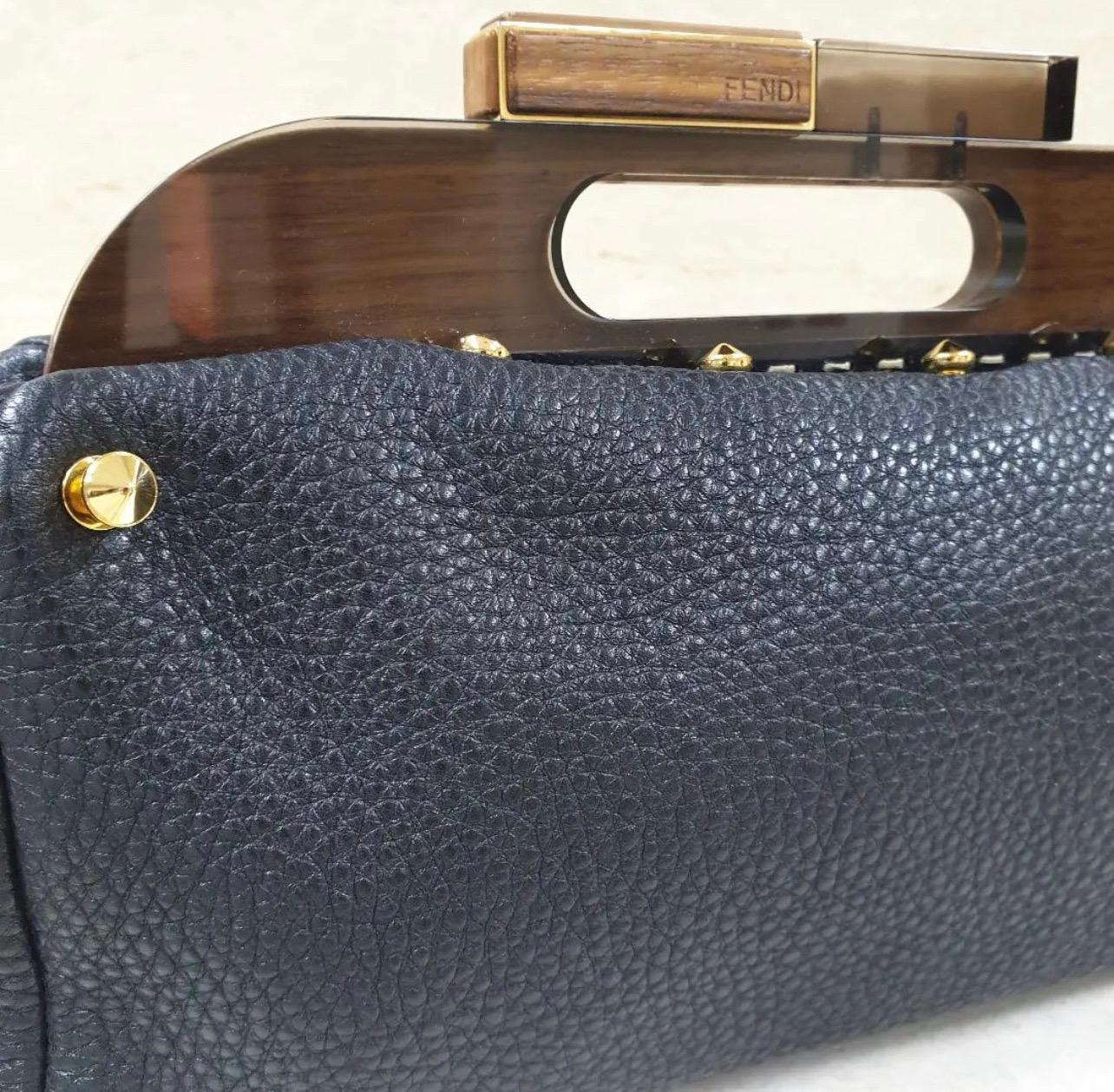 This sleek and vintage-inspired Fendi Black Leather Walnut Wood Handle Clutch Bag is the perfect accessory for going out or traveling light. The rounded profile gives this clutch an ultra-spacious interior and the wooden handle allows for easy