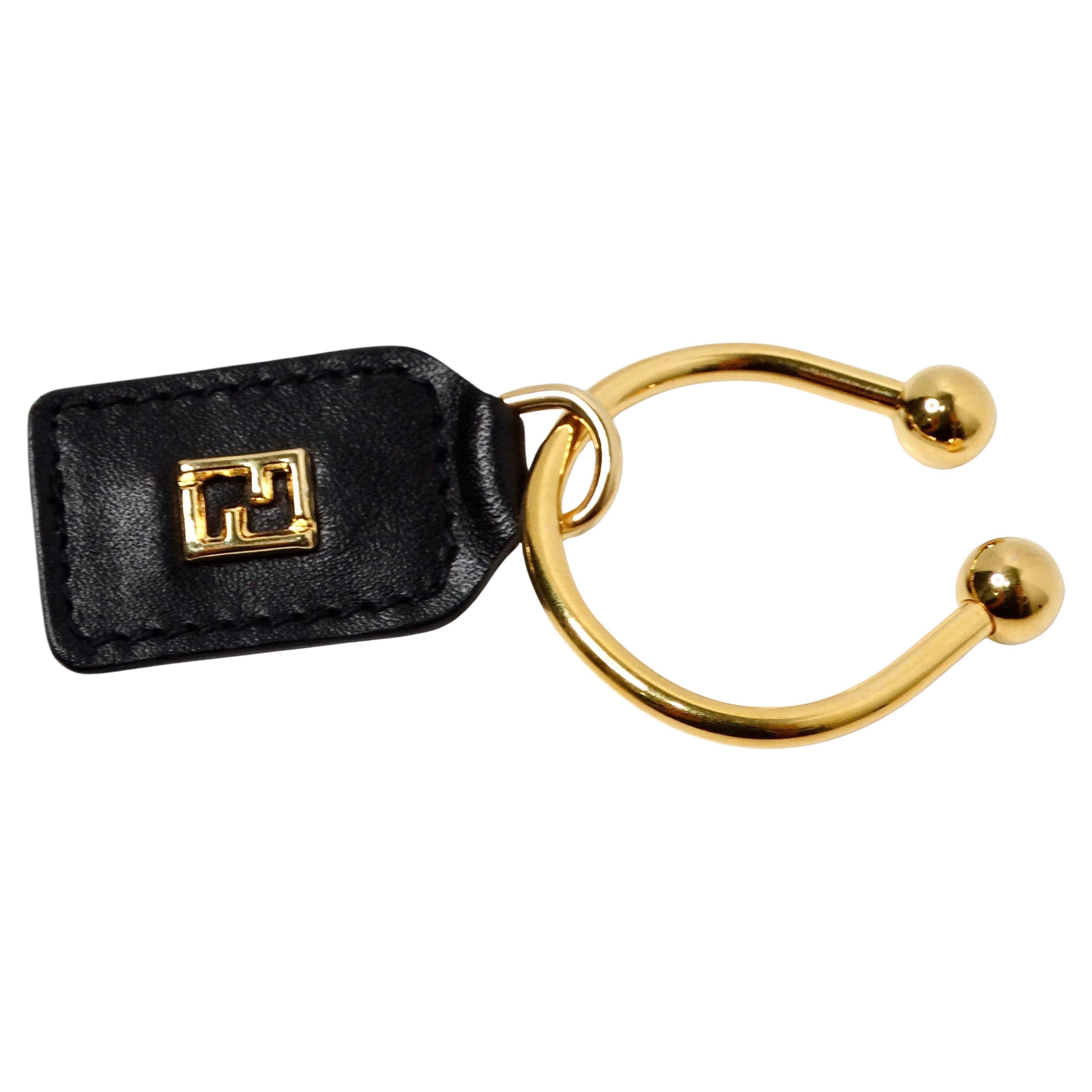 Il portachiavi con logo Fendi in pelle nera e oro giallo è un accessorio di lusso che unisce perfettamente raffinatezza e praticità. Realizzata in elegante pelle nera, emana un'eleganza senza tempo, mentre il logo FF Fendi in oro giallo aggiunge un