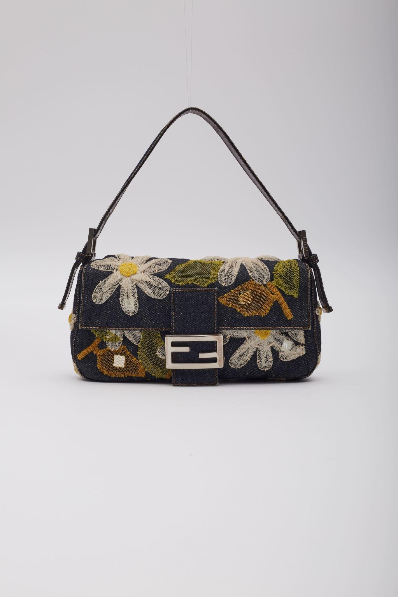 This baguette is made of denim with a bold stitching around all borders. The bag features mesh floral embroidery, a looping leather shoulder strap with silver hardware, and a full frontal flap with a silver Fendi FF logo. The flap opens with a