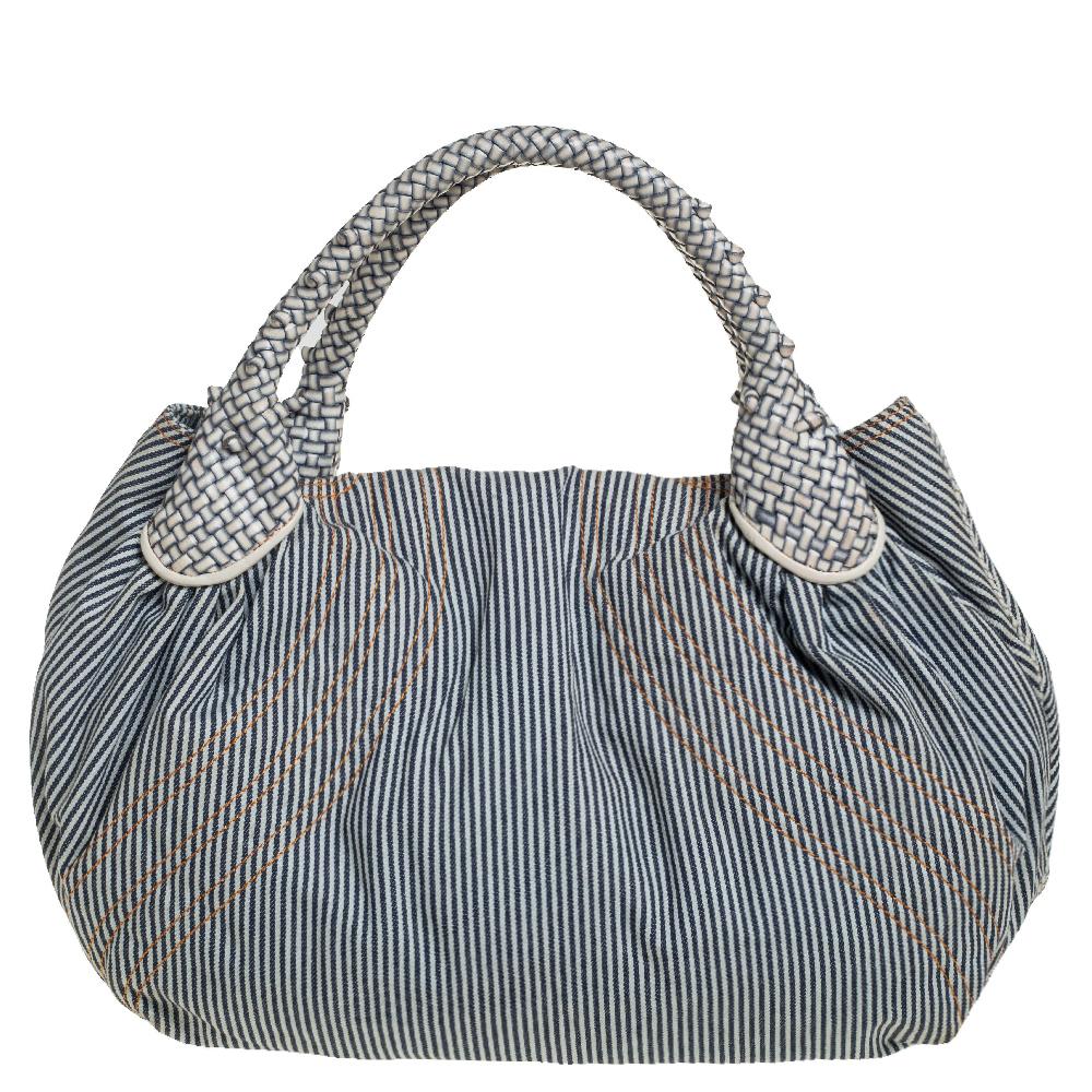 Este elegante bolso Spy es de Fendi. El bolso está confeccionado en tejido de rayas con adornos de piel y dos asas tejidas en la parte superior. La bolsa también viene con un interior de tela en el que caben todos tus objetos cotidianos. Presume de
