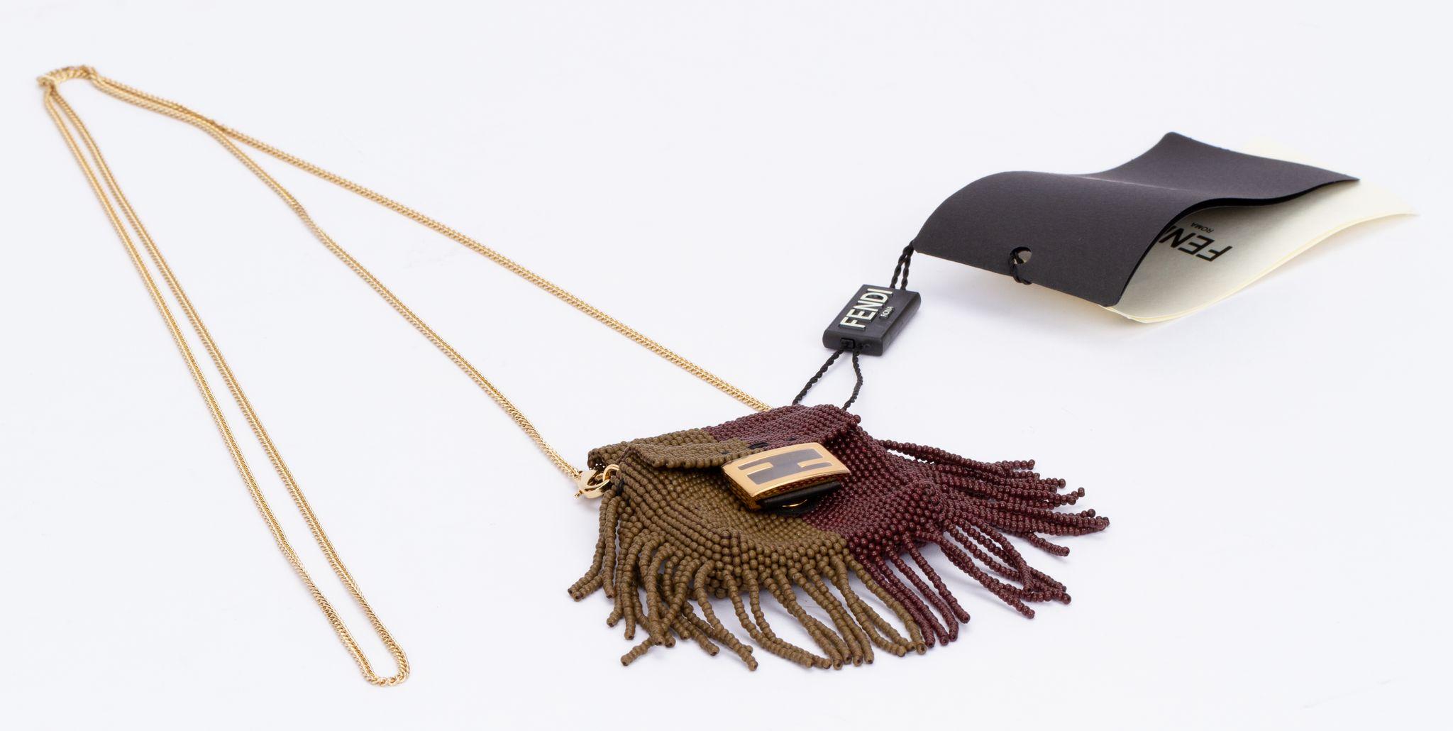 Fendi micro necklace baguette with tassels. The bag is made of beaded fabric in the colors brown and olive. Attached on it are tassels. The piece can be worn as a necklace as well as a mini bag or be attached to a bigger bag. The chain is detachable