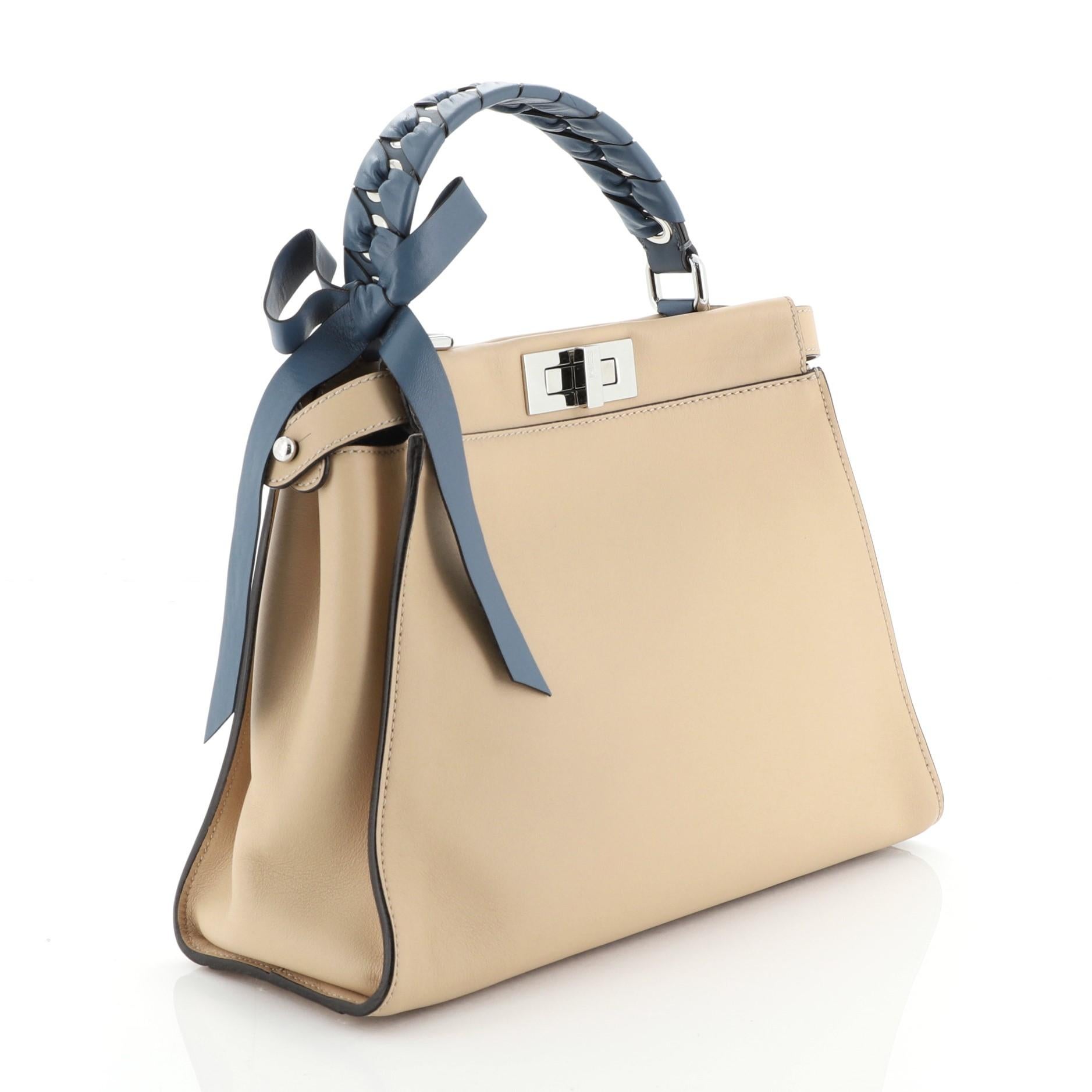 This Fendi Bow Peekaboo Bag Whipstitch Leather Regular crafted from neutral leather with whipstitch detailing, features a top frame silhouette, flat leather handle, and silver-tone hardware. Its turn-lock closure opens to a neutral leather and blue