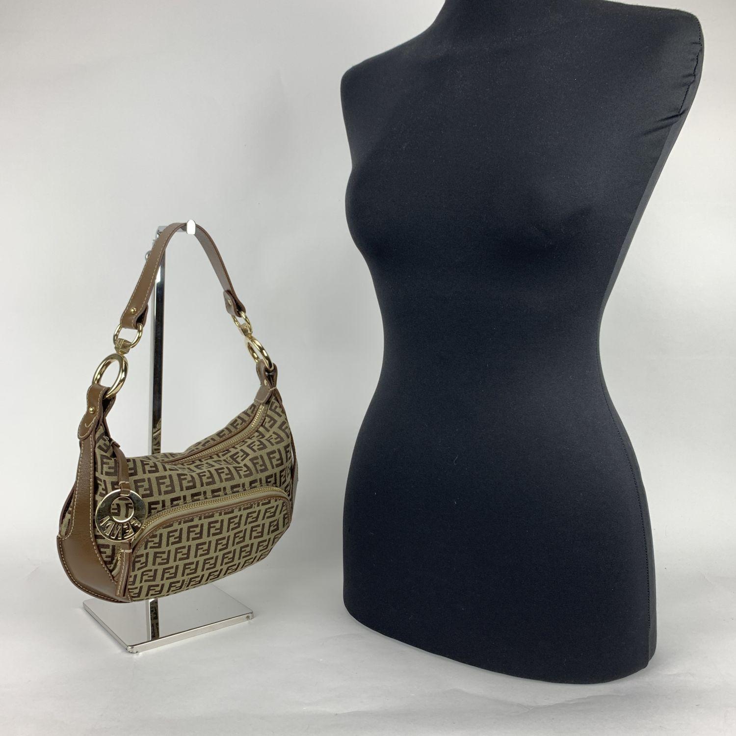 Fendi Hobo Bag made in FF monogram Zucchino canvas with genuine leather trim and shoulder strap in brown color. Gold metal FF - FENDI cut out logo zipper pull. Upper zipper closure. Front zip pocket. Brown fabric lining with 1 side open pocket