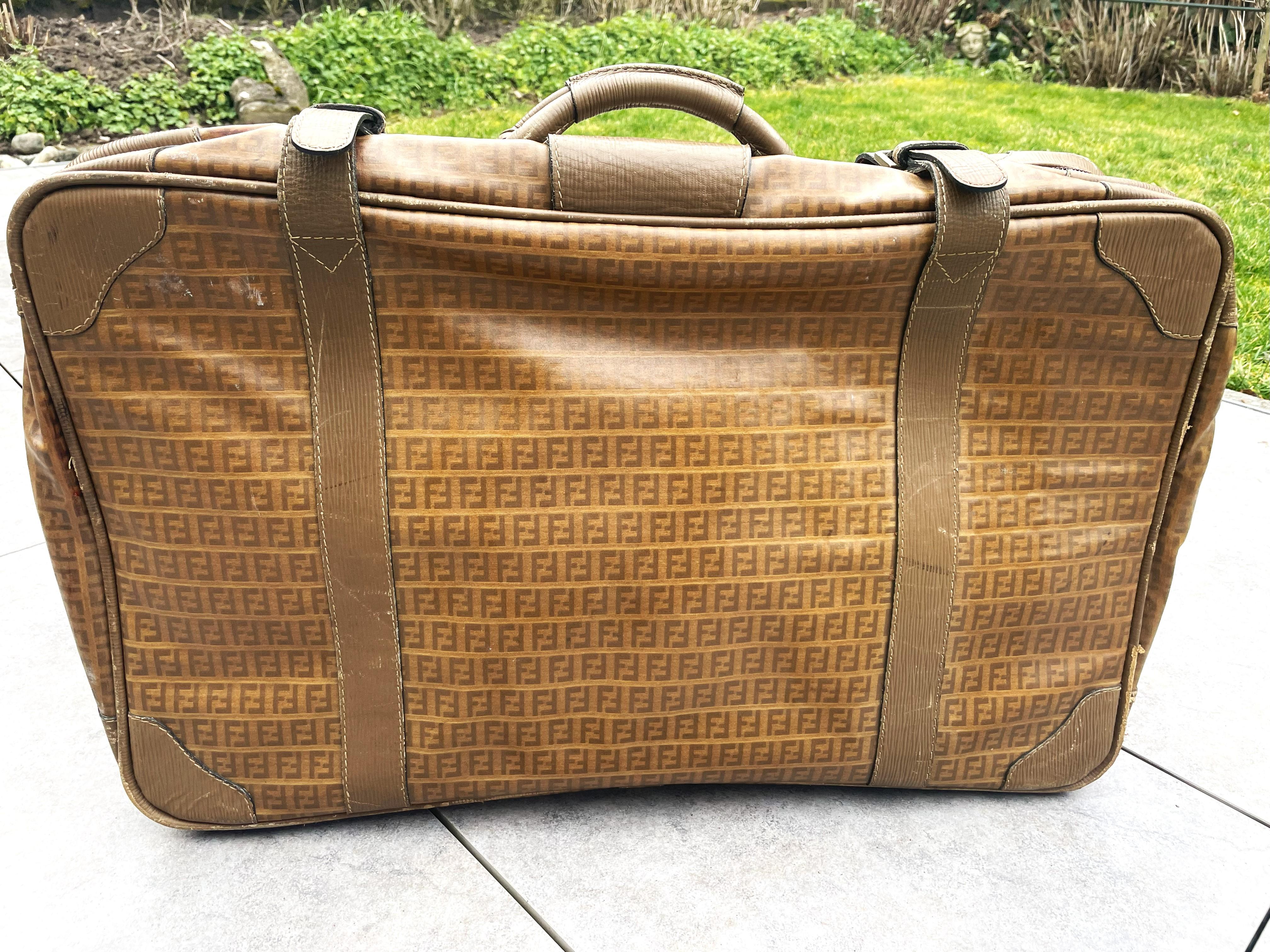 The classic FENDI Zucca FF Monogram suitcase made of canvas and leather.
 Leather handle, corners and case strap. Inside lined with brown fabric, a long compartment on the side with a zipper and leather strap. Very good condition inside, no