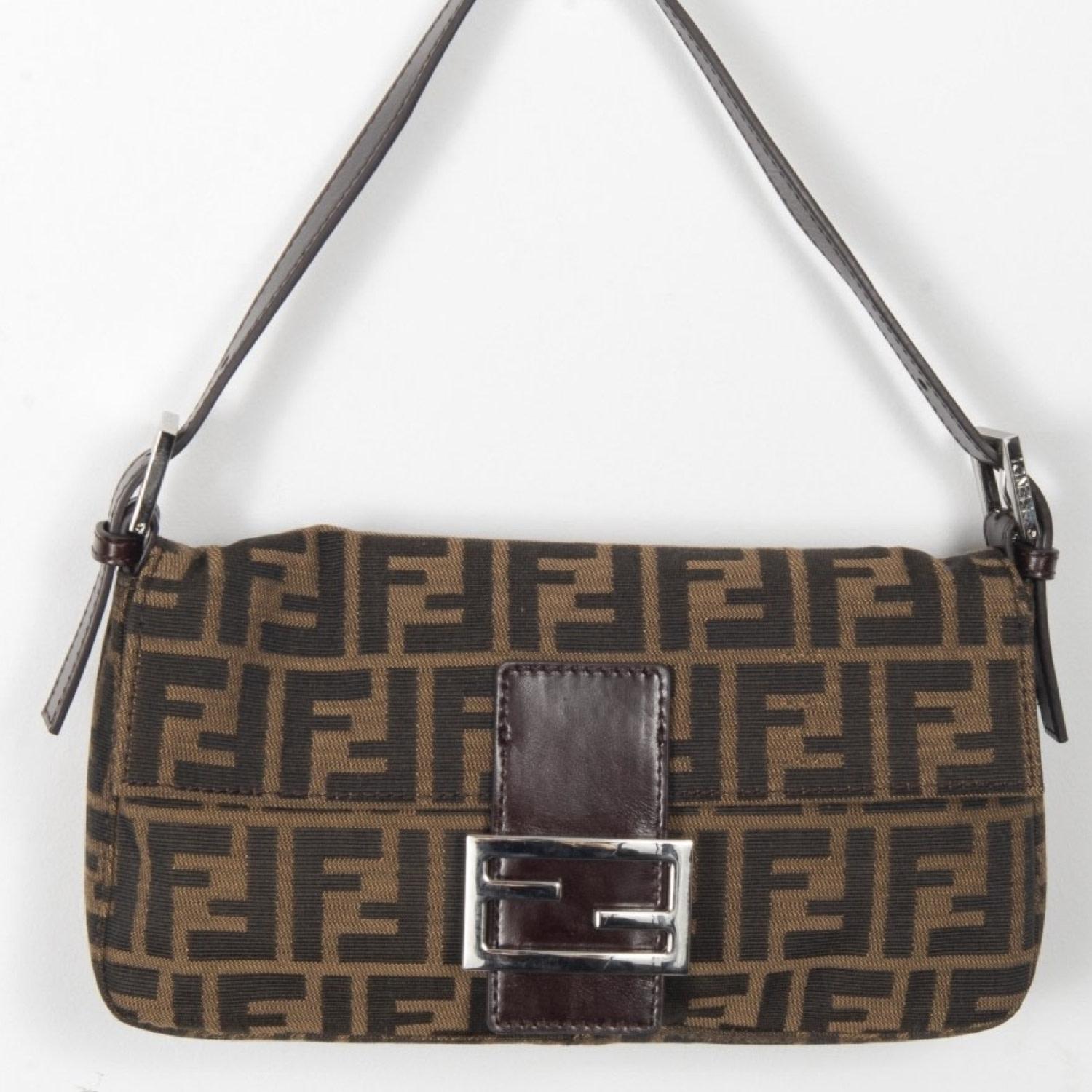 The Fendi baguette is one of the brands most iconic styles. This particular one features the Fendi Zucca monogram print on canvas with leather handles, leather trim and brown fabric interior lining. A metal Fendi logo on the front flap with snap