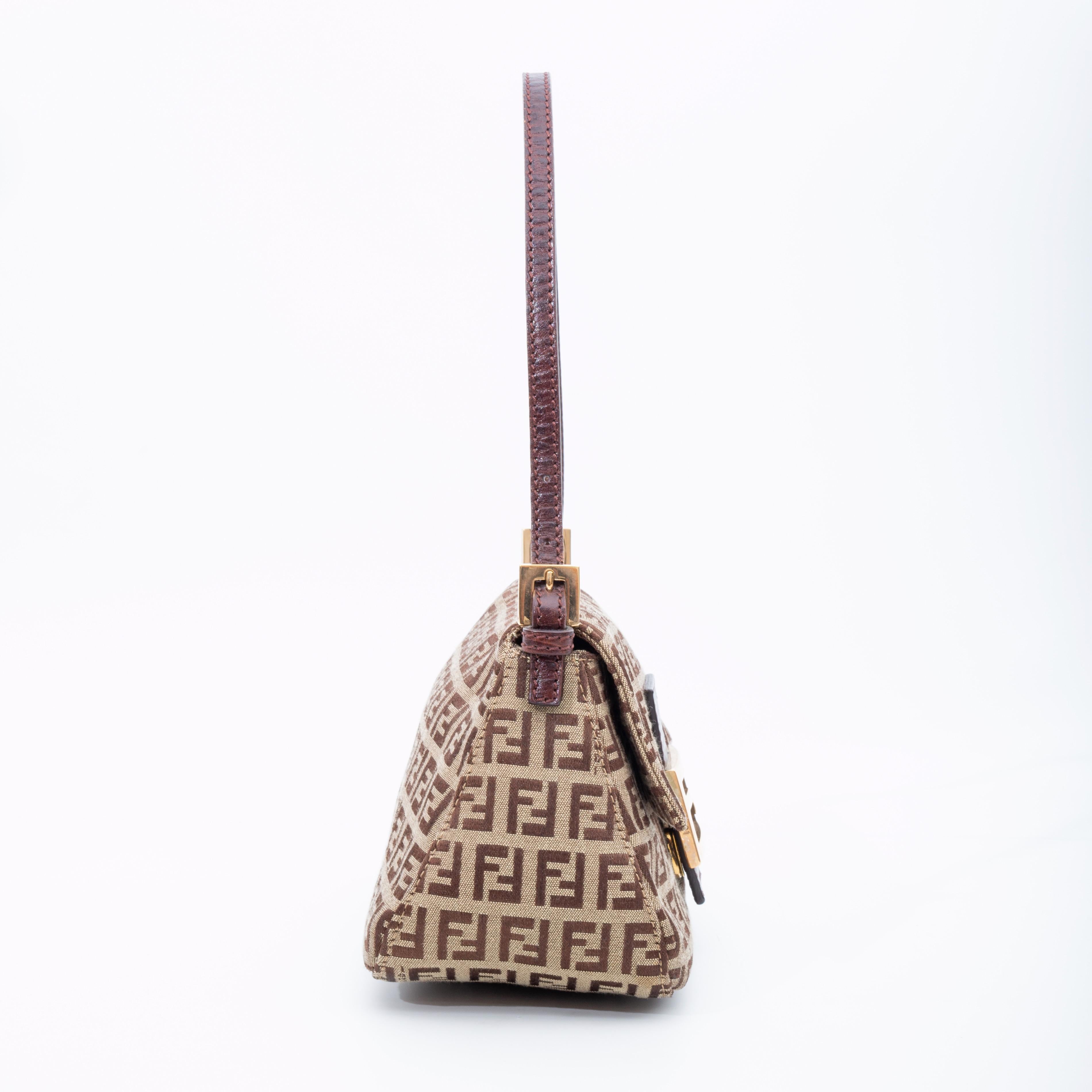 This mini baguette bag is made of Fendi zucchino canvas in light brown/beige. The bag features a brown flat leather shoulder strap attached by gold tone links, a flap with a polished gold FF logo, snap closure on flap buckle, and brown fabric