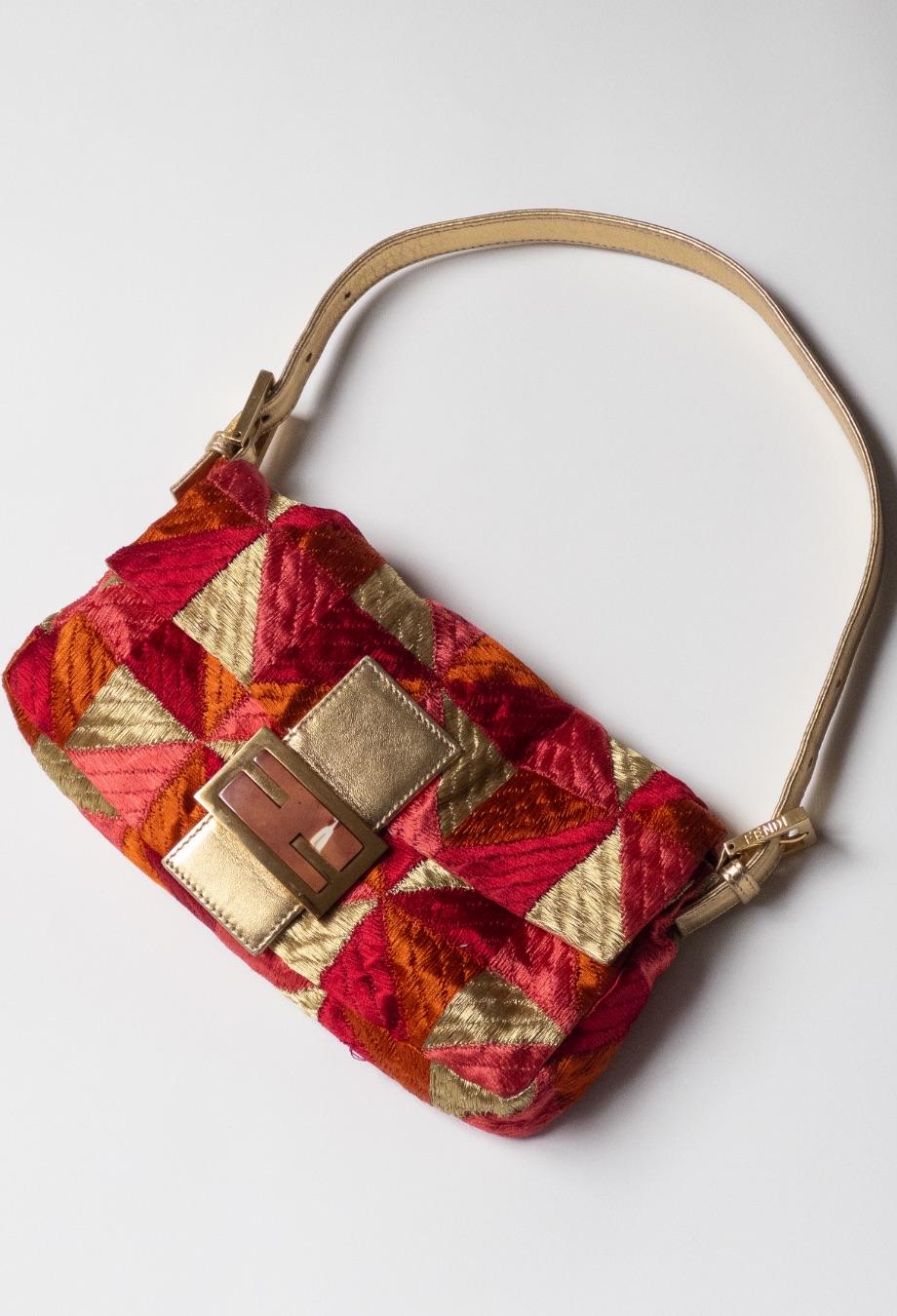 Fendi’s iconic baguette bag receives a bold update with this vibrant, embroidered iteration. Crafted from luxurious threads, it showcases a geometric patchwork design in opulent hues of red, orange, and gold, offering a rich, tactile finish. The