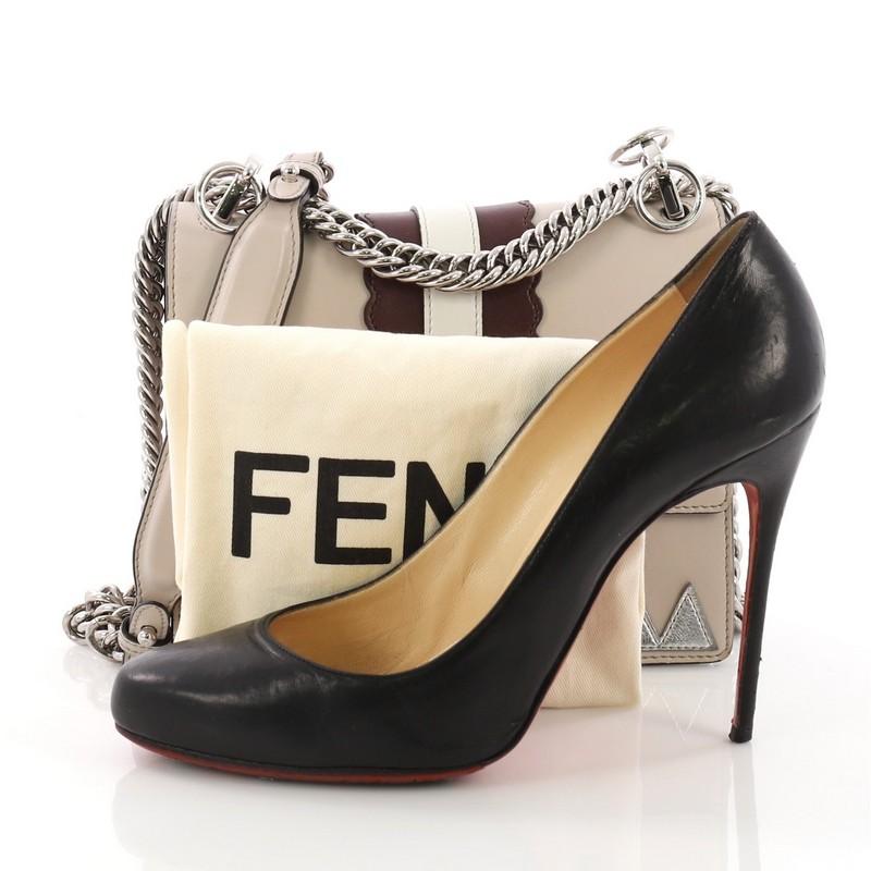 This Fendi Faces Kan I Handbag Leather Small, crafted from gray leather, features long sliding chain-link shoulder strap with leather insert, eyes-stud embellishments, double stud two-tone plexiglass twist-lock closure, and silver-tone hardware. Its