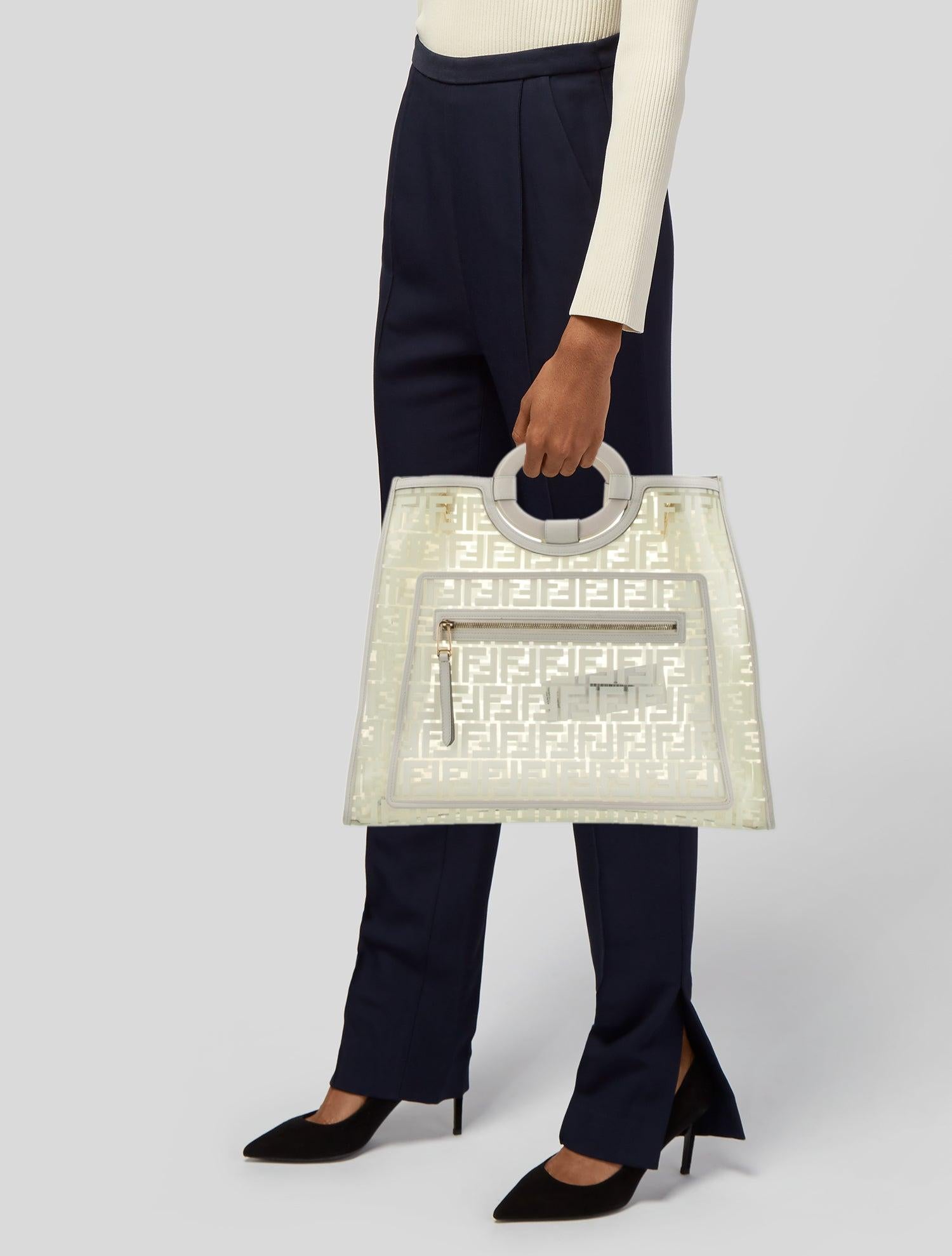 This Fendi top handle bag features transparent PVC construction, white Zucca FF print throughout, gold-tone hardware, leather trim embellishment and is complete with an open top.

Size Medium
Color: White print / transparent
Material: PVC with