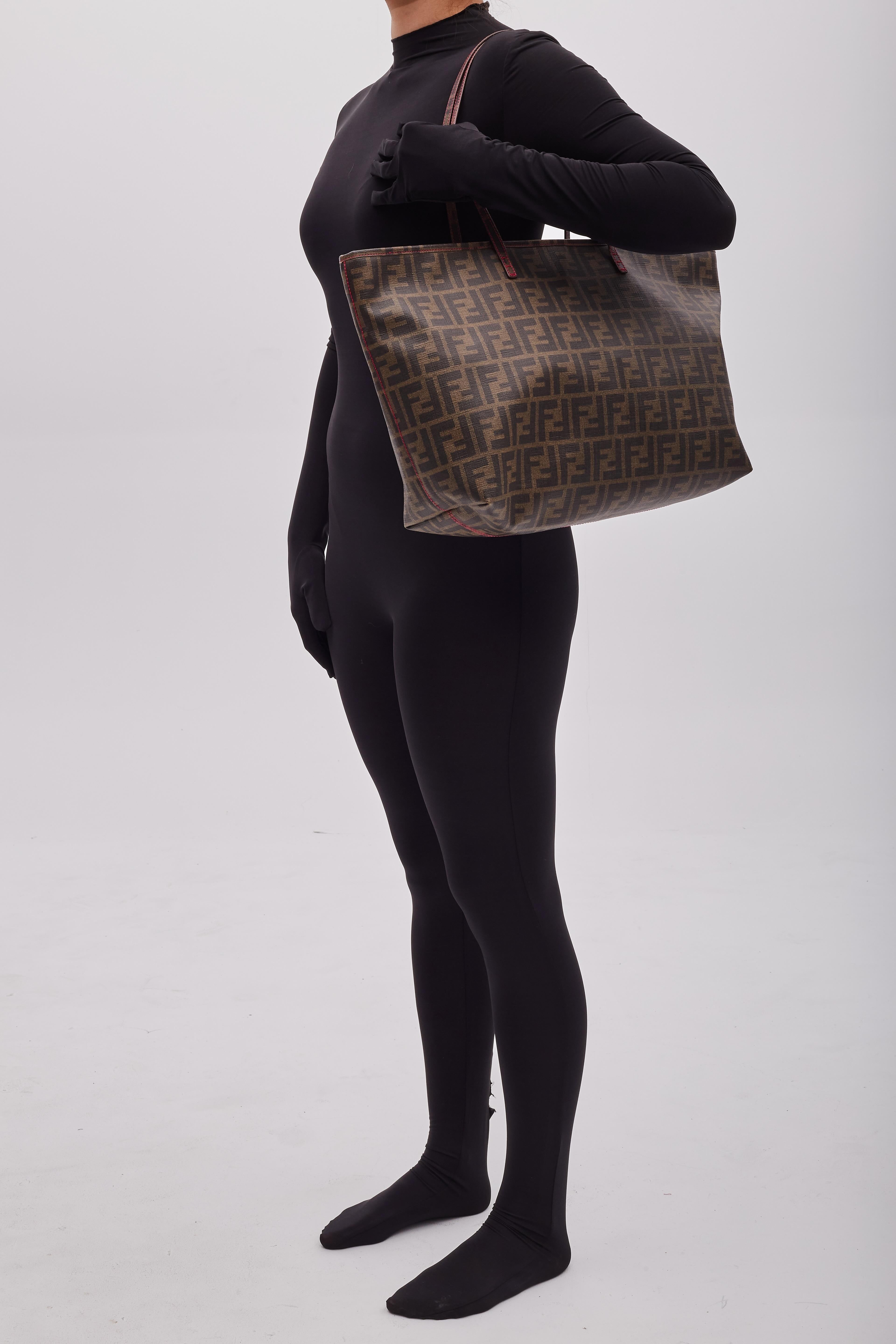 Fendi tote bag from the 2011 collection. This bag is made of coated canvas in brown/ebony with monogram Zucca print throughout. The bag features gold-tone hardware, dual flat leather shoulder straps, an open top and fuchsia stitching details. The
