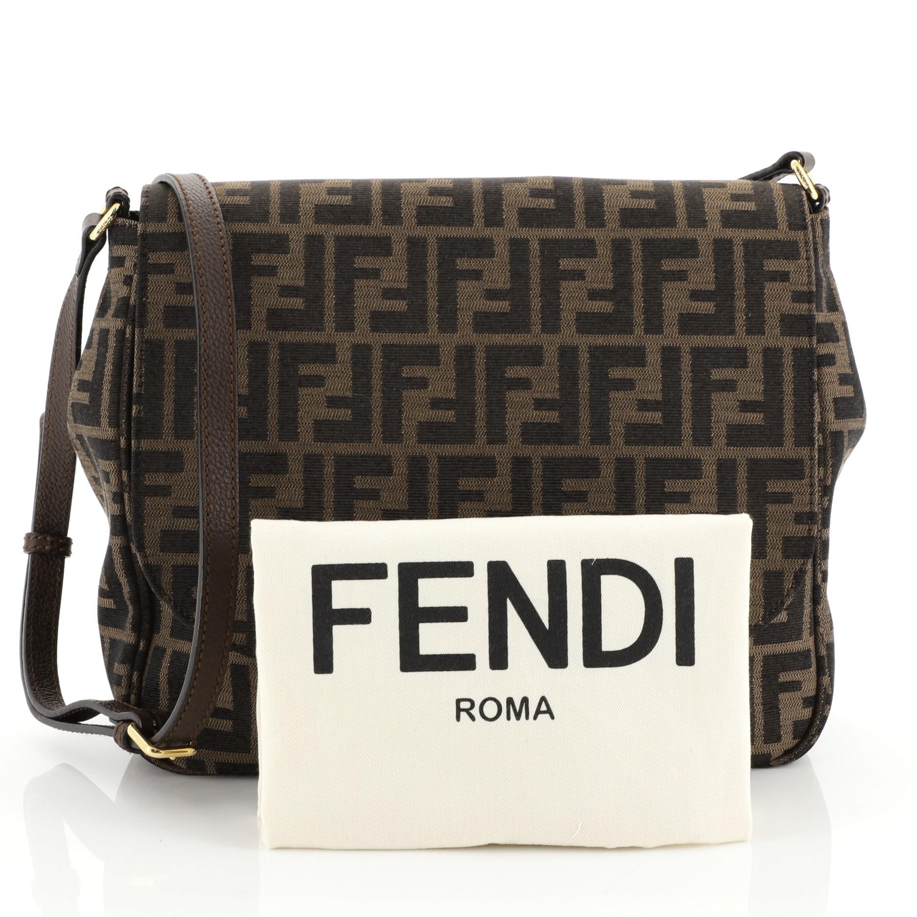 This Fendi Flap Crossbody Bag Zucca Canvas Medium, crafted from brown zucca coated canvas, features an adjustable strap, frontal flap, exterior slip pocket and gold-tone hardware. Its magnetic snap closure opens to a black fabric interior with slip