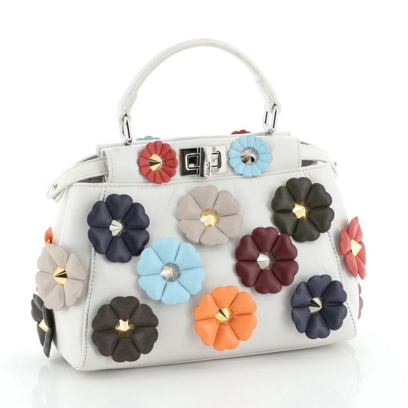 This Fendi Flowerland Peekaboo Bag Embellished Leather Mini, crafted from white leather, features short leather top handle, protective base studs, and silver-tone hardware. Its two compartments with turn-lock and zip closures open to a white leather