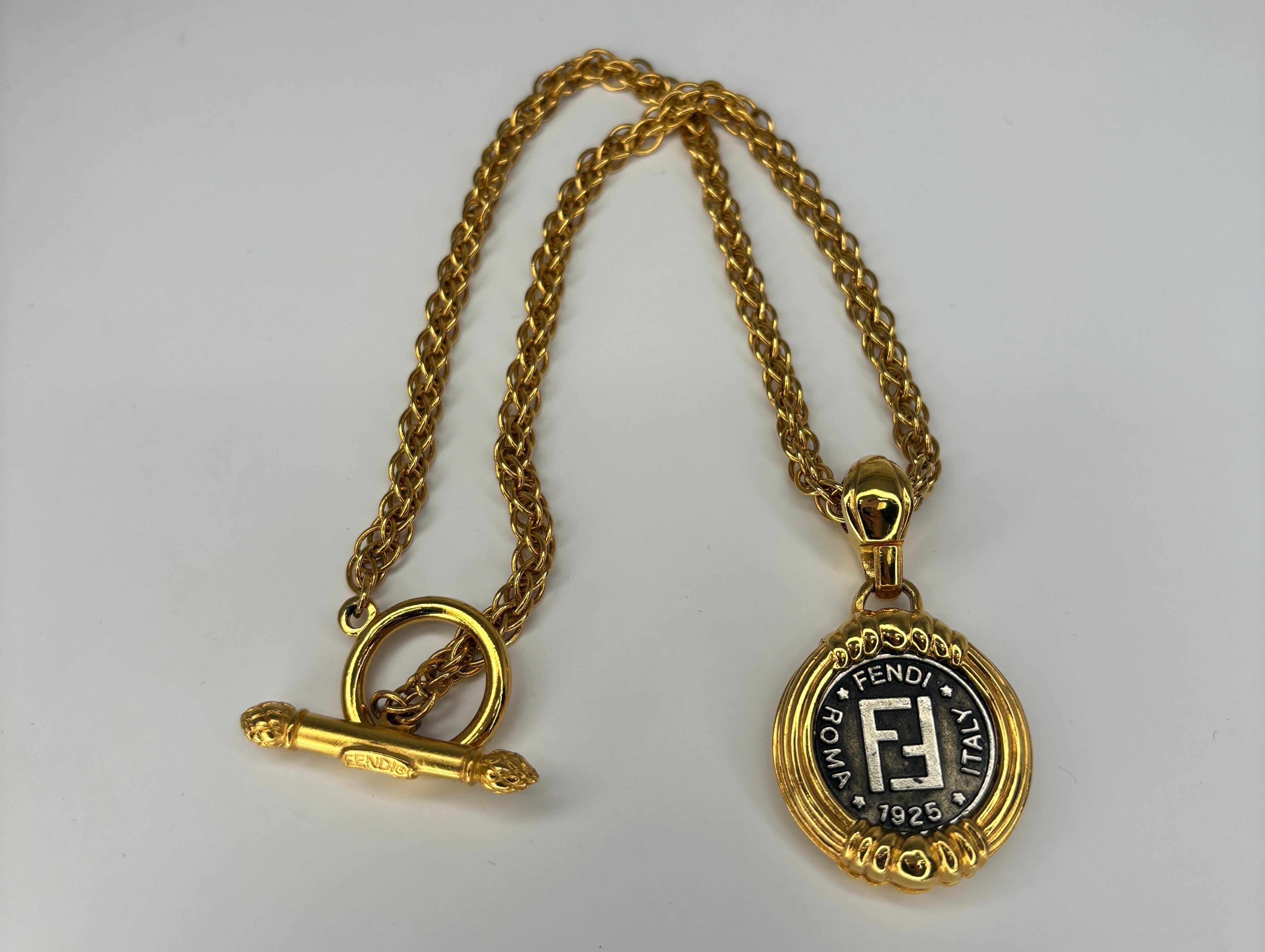 This Fendi's Coin Pendant Necklace is a distinctive piece from the renowned Italian luxury fashion house known for its elegance, craftsmanship, and innovation. The centerpiece of this necklace is a coin pendant featuring double-sided designs, which