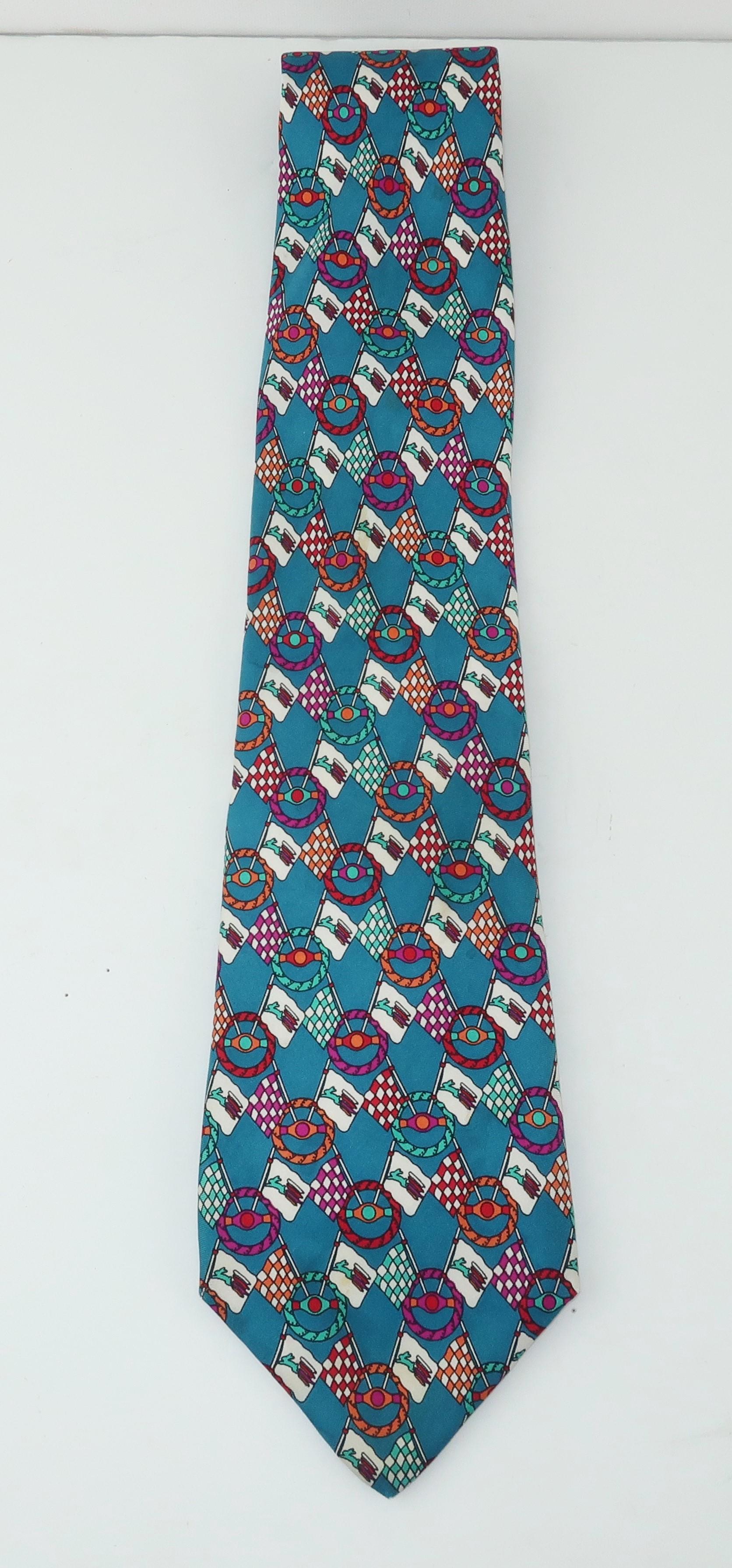 Fendi creates a colorful men’s silk necktie with a racing flag and steering wheel motif.  White, fuchsia, red, aqua and orange pop off of a brilliant blue background.  Fair previously owned condition with some subtle discolorations shown in