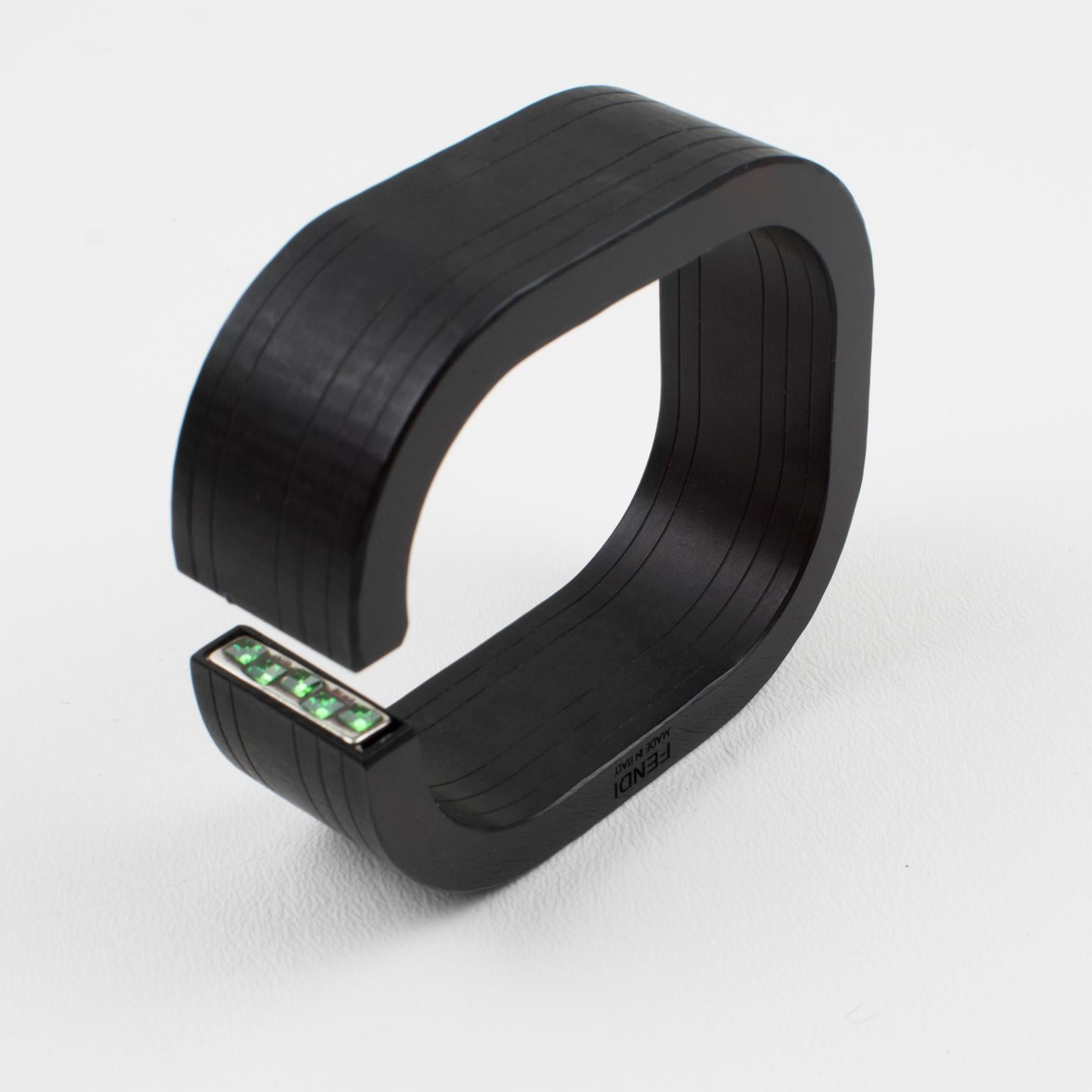 This stunning Fendi, Italy acrylic resin bracelet features a geometric bangle with a square cuff shape in true licorice black, adorned with two sterling silver plaques set with square green crystal rhinestones inside the cuff opening. The engraved