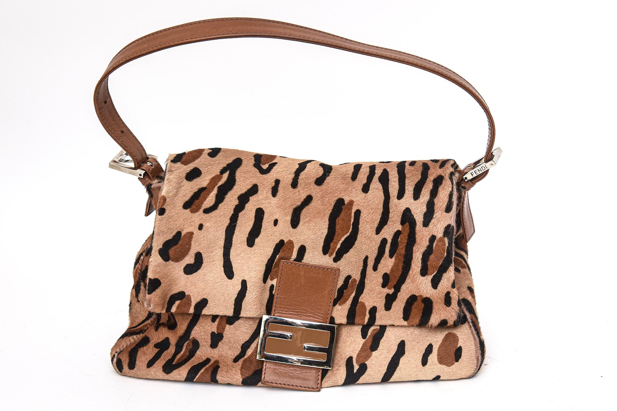 This chic and lovely Fendi leopard print pony hair mama baguette handbag has a tan leather handle with a closure flap. The metal hardware is silver. It was from the 1990's. It comes with the original duster with draw strings in gold metal and the
