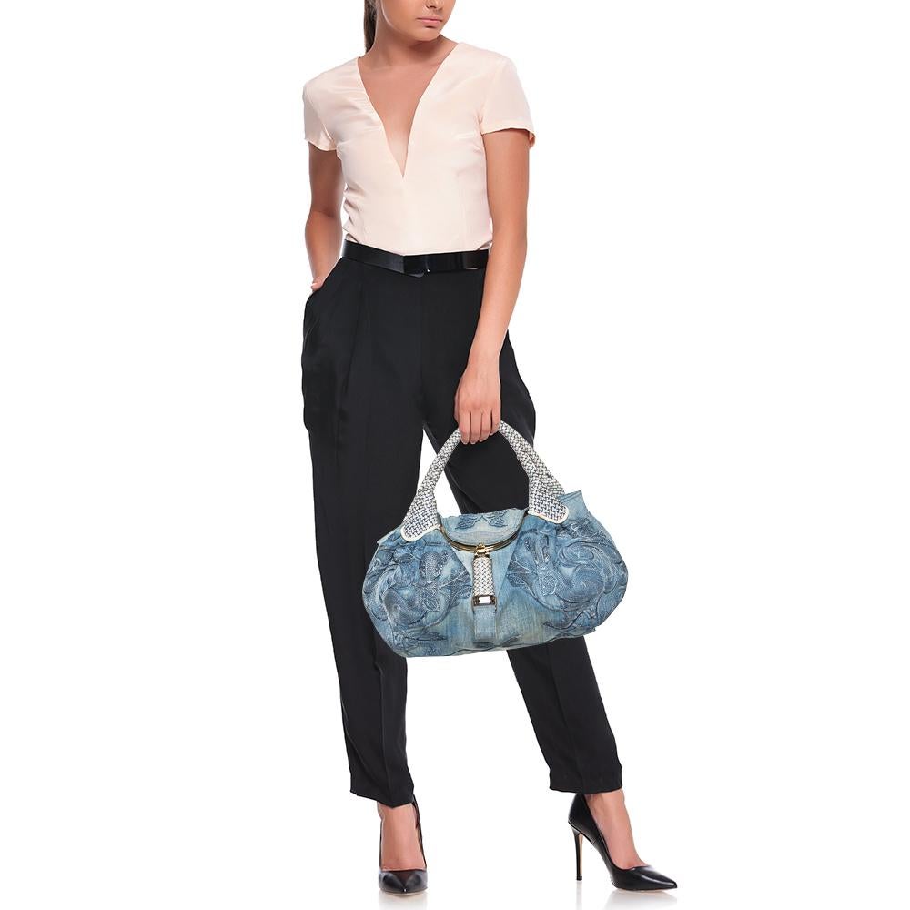 Este hobo de edición limitada de Fendi es una creación que no te puedes perder. Femenino, elegante y práctico, está confeccionado en tela vaquera azul y presenta un intrincado bordado en el exterior. La pieza está adornada con dos asas y una solapa