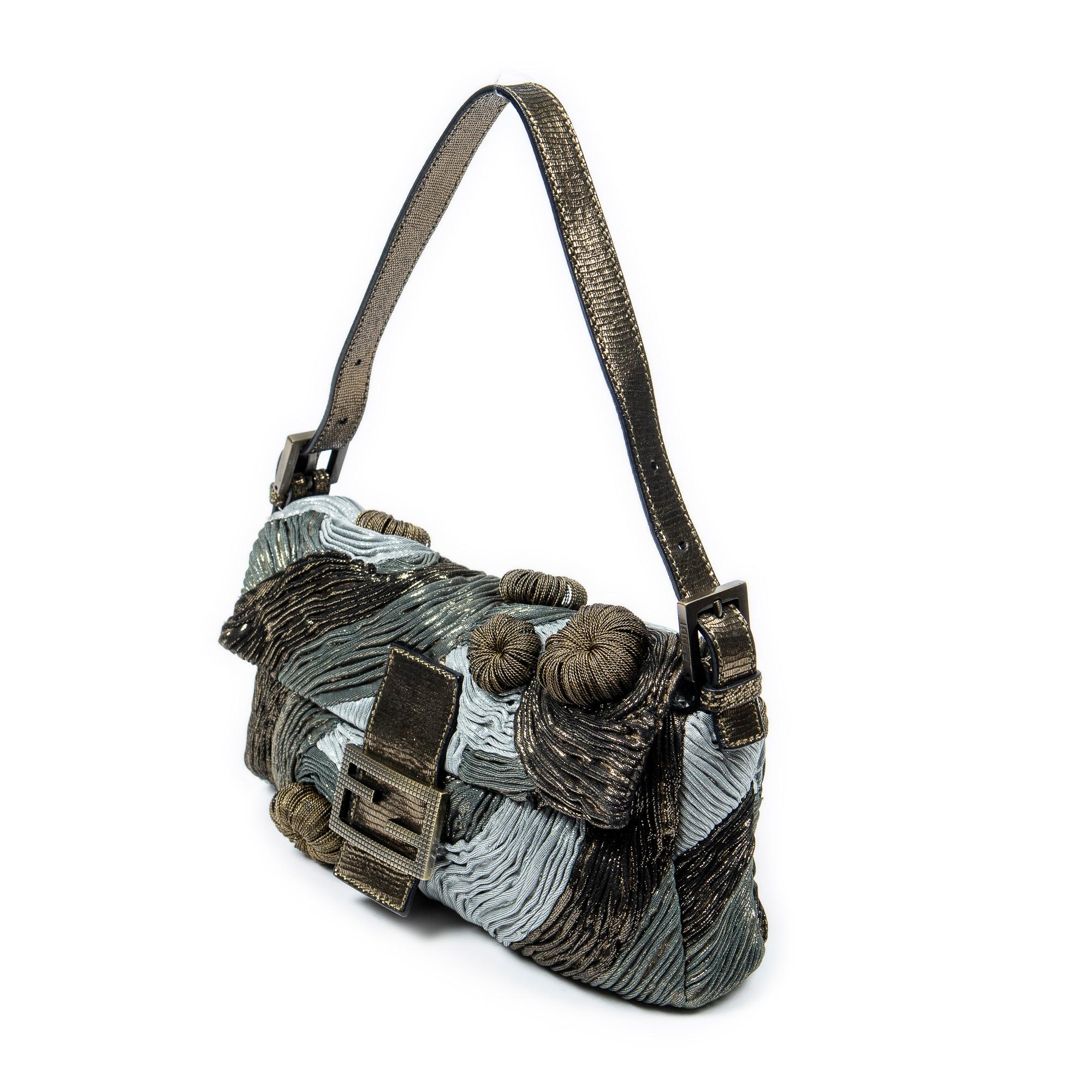 Embellish your style with the Olive/Blue/Green Ltd. Ed. Metallic Medusa Baguette, featuring a captivating olive/blue/green metallic-thread lined canvas. Its brushed gold hardware and satin closure radiate elegance while the interior zippered pocket