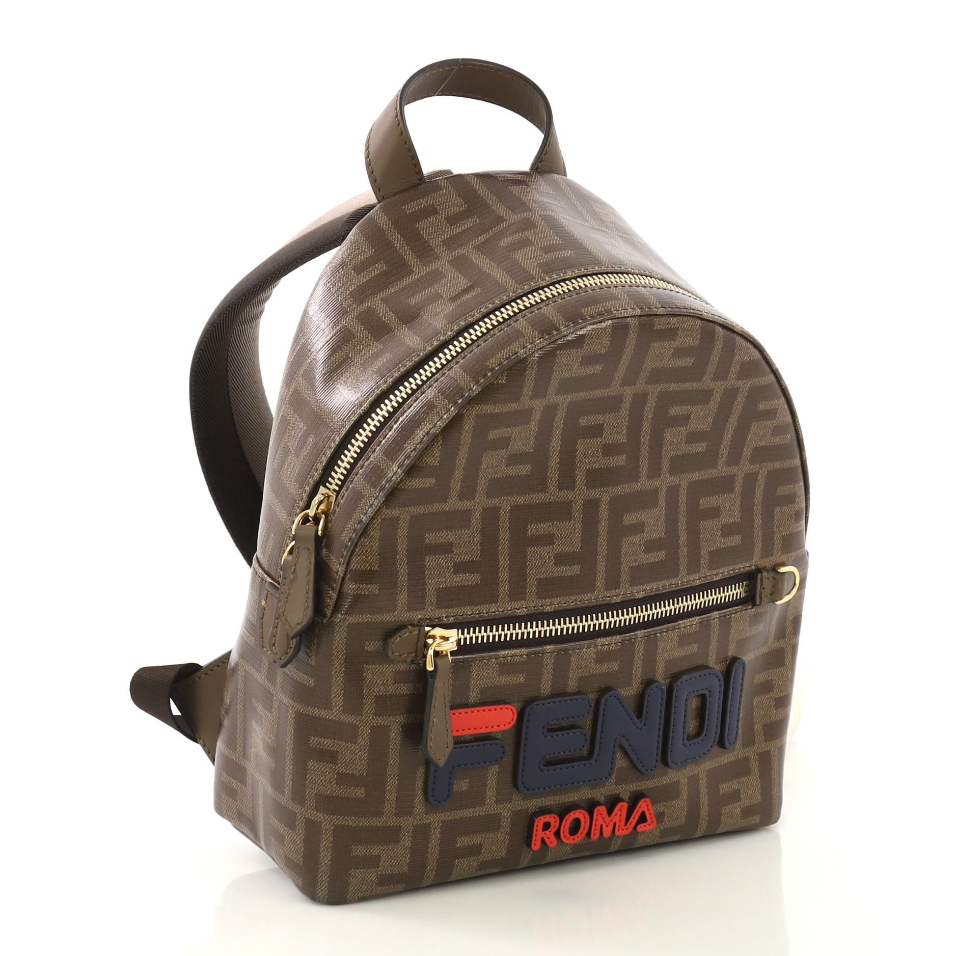 This Fendi Mania Logo Backpack Zucca Coated Canvas, crafted from brown zucca coated canvas, features adjustable shoulder straps, front zip pocket, and gold-tone hardware. Its zip closure opens to a brown fabric interior with zip pocket. 

Estimated