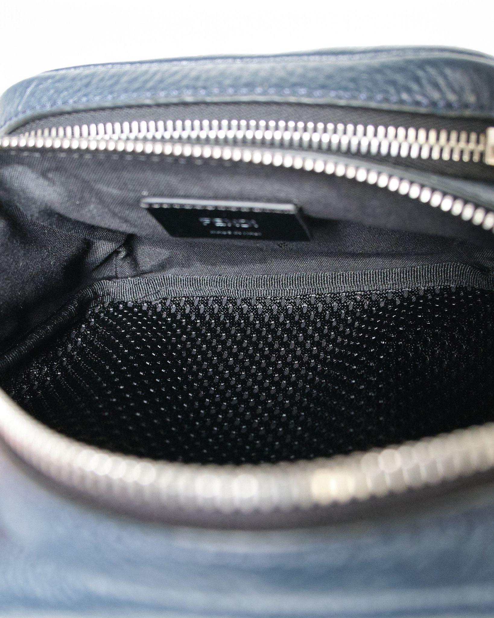 Fendi signature fanny pack, model Monster, made of grained leather in midnight blue color with black inserts and silver hardware details. The semi-circular zipper closure opens to a black fabric-lined interior with a convenient pocket perfect for