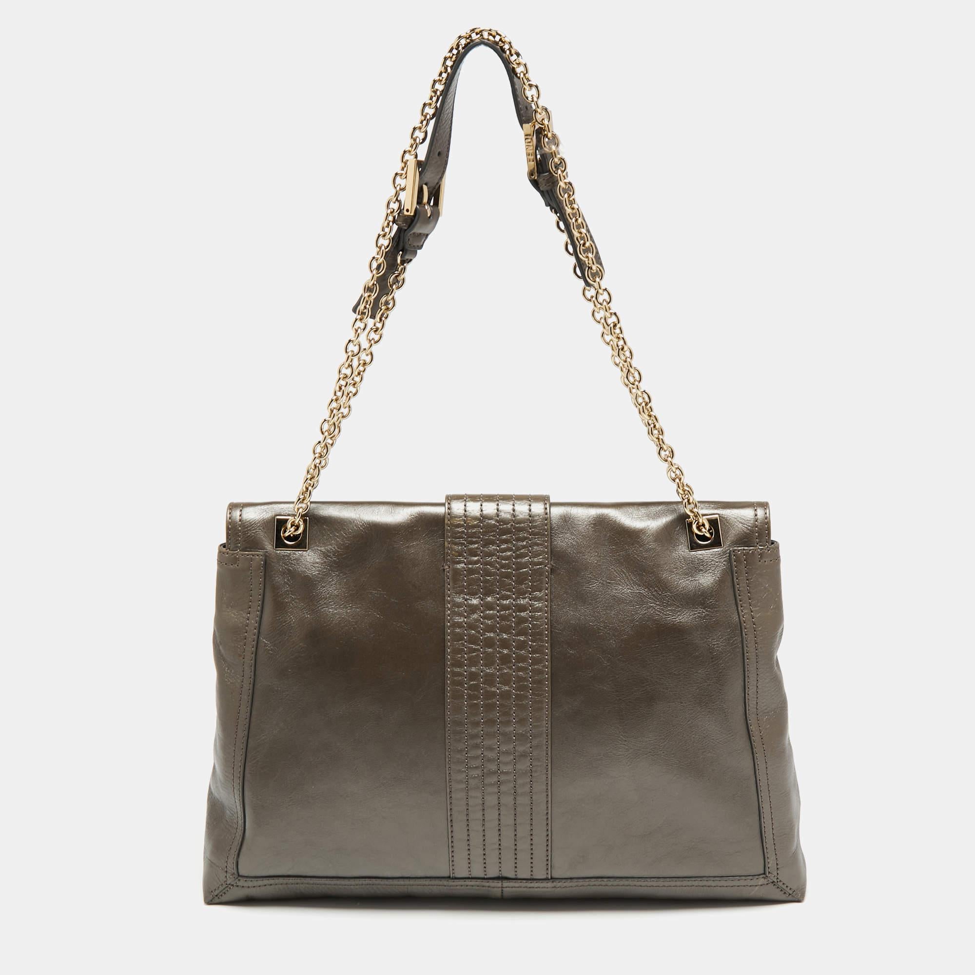 This Maxi Baguette Flap shoulder bag designed by the House of Fendi offers never-ending functionality and luxury! It is made from grey leather with a gold-tone FF accent placed on the front. It accommodates a spacious fabric-lined interior. Grab