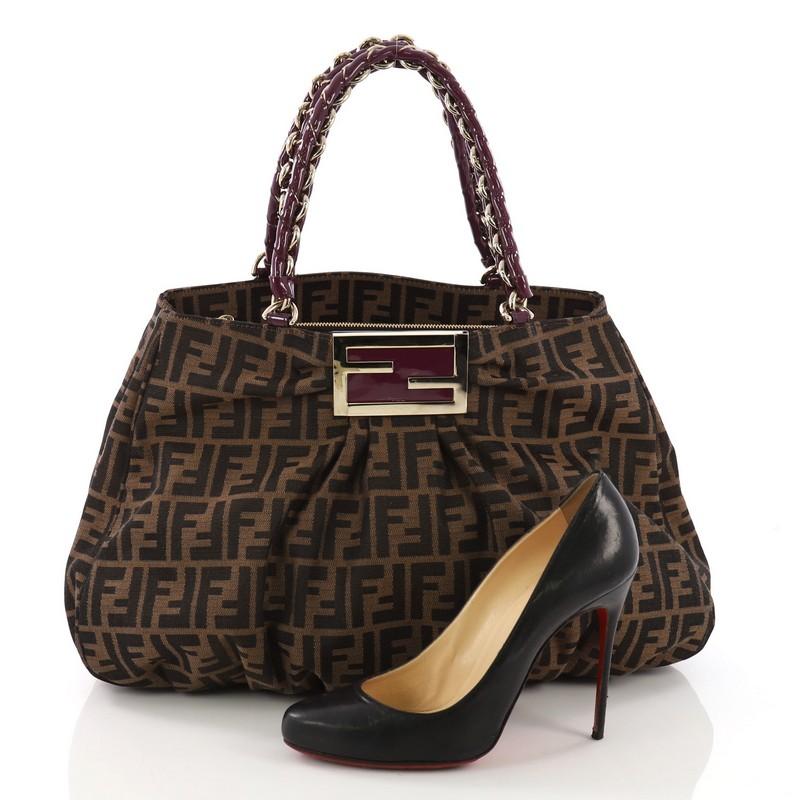 This Fendi Mia Tote Zucca Canvas Large, crafted from brown zucca canvas, features woven-in leather chain handles, intricate pleating, giant Fendi logo and gold-tone hardware. Its wide top opening showcases a purple fabric interior with middle zip