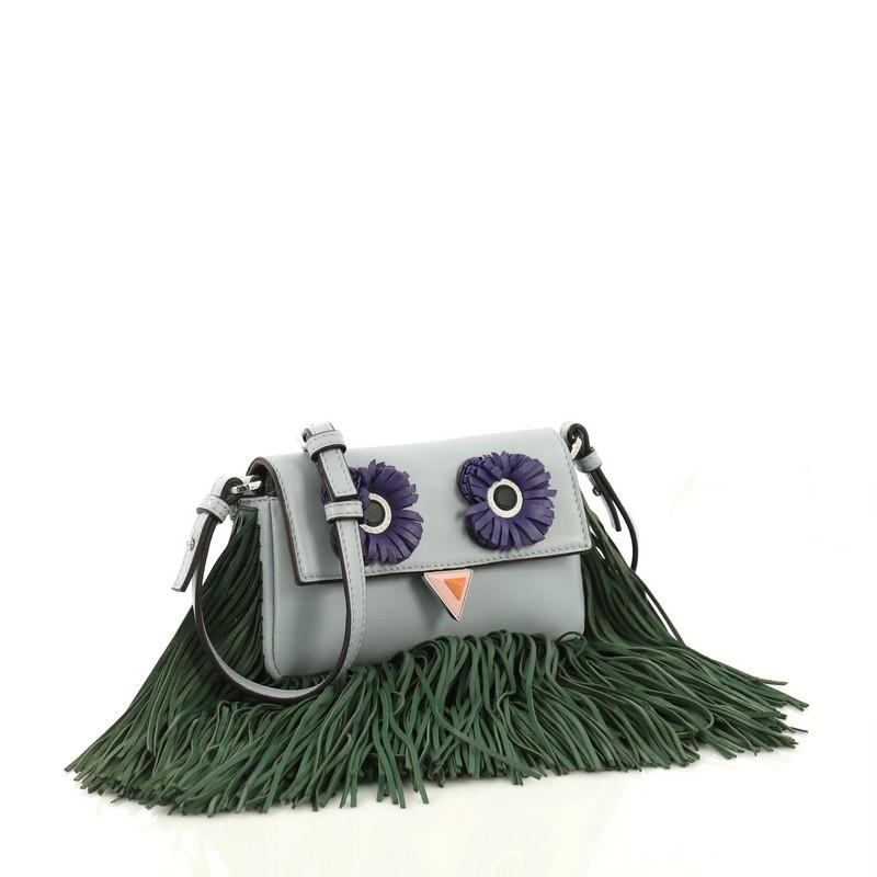 This Fendi Monster Baguette Fringe Leather Micro, crafted from blue leather, features flat leather strap, fringe accents at base, monster eyes at front, and silver-tone hardware. Its magnetic snap closure opens to a gray microfiber interior with