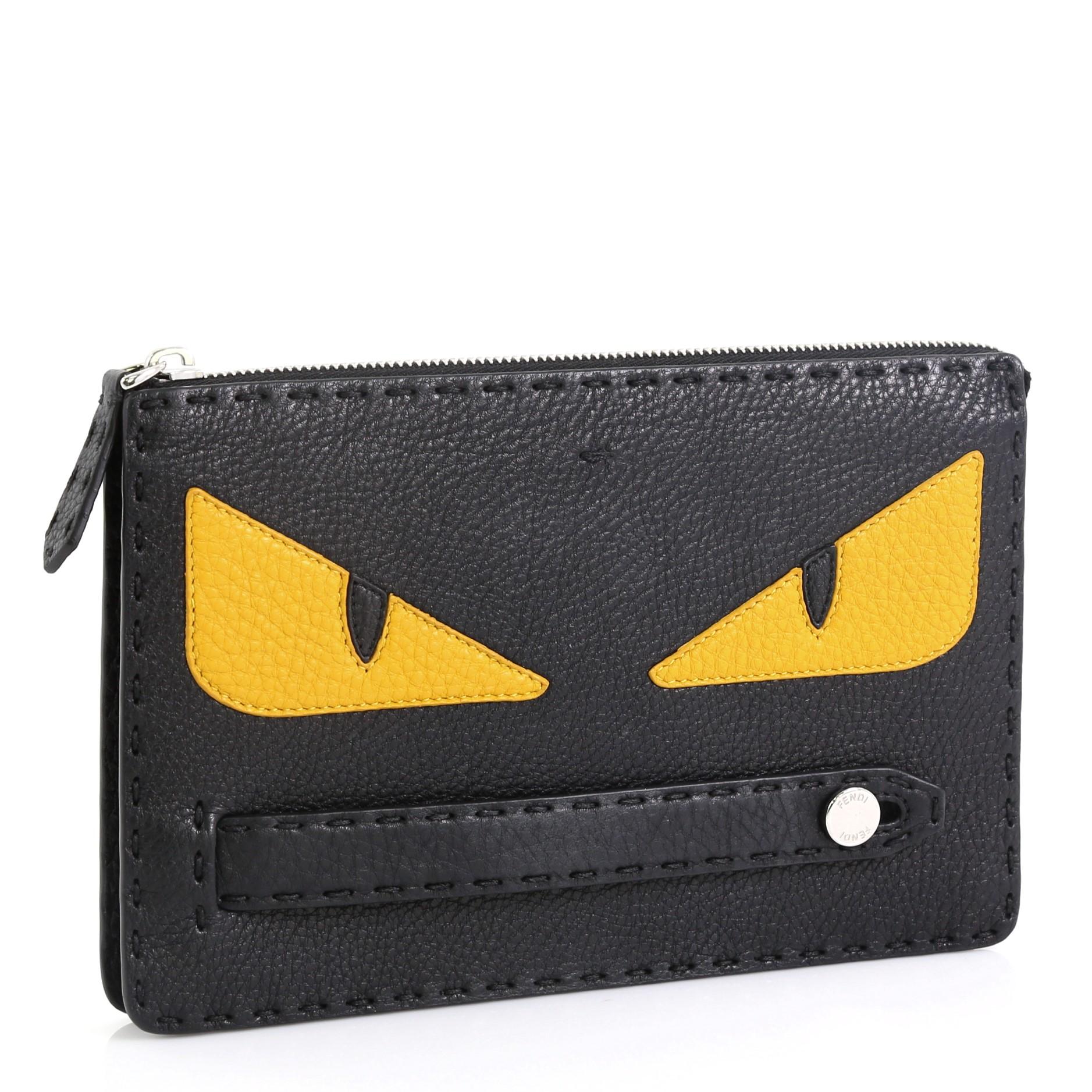 This Fendi Monster Clutch Selleria Leather Small, crafted from black and yellow leather, features a leather handle strap, Fendi's monster design, and silver-tone hardware. Its zip closure opens to a black fabric and leather interior with multiple