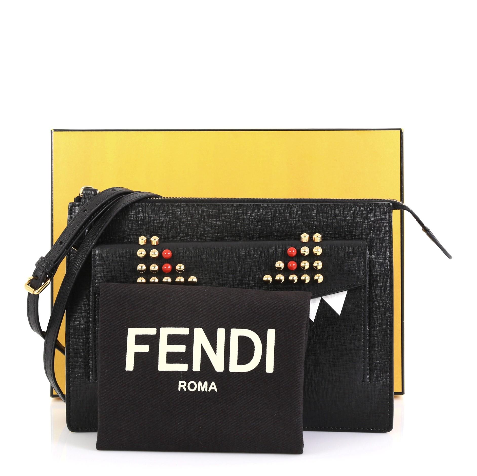 This Fendi Monster Crossbody Bag Leather, crafted from black leather, features adjustable crossbody strap, exterior front flap pocket, monster design with painted teeth, gold and red studded eyes, and gold-tone hardware. Its zip closure opens to a