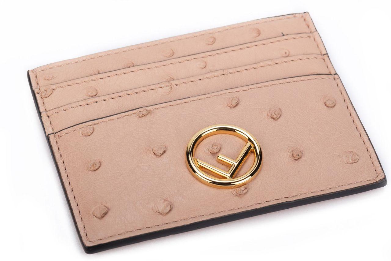 Fendi card holder in powder pink crafted of ostrich leather. On the front is singular F in gold. The holder has three card departments. It is brand new and comes with the box and dustcover.