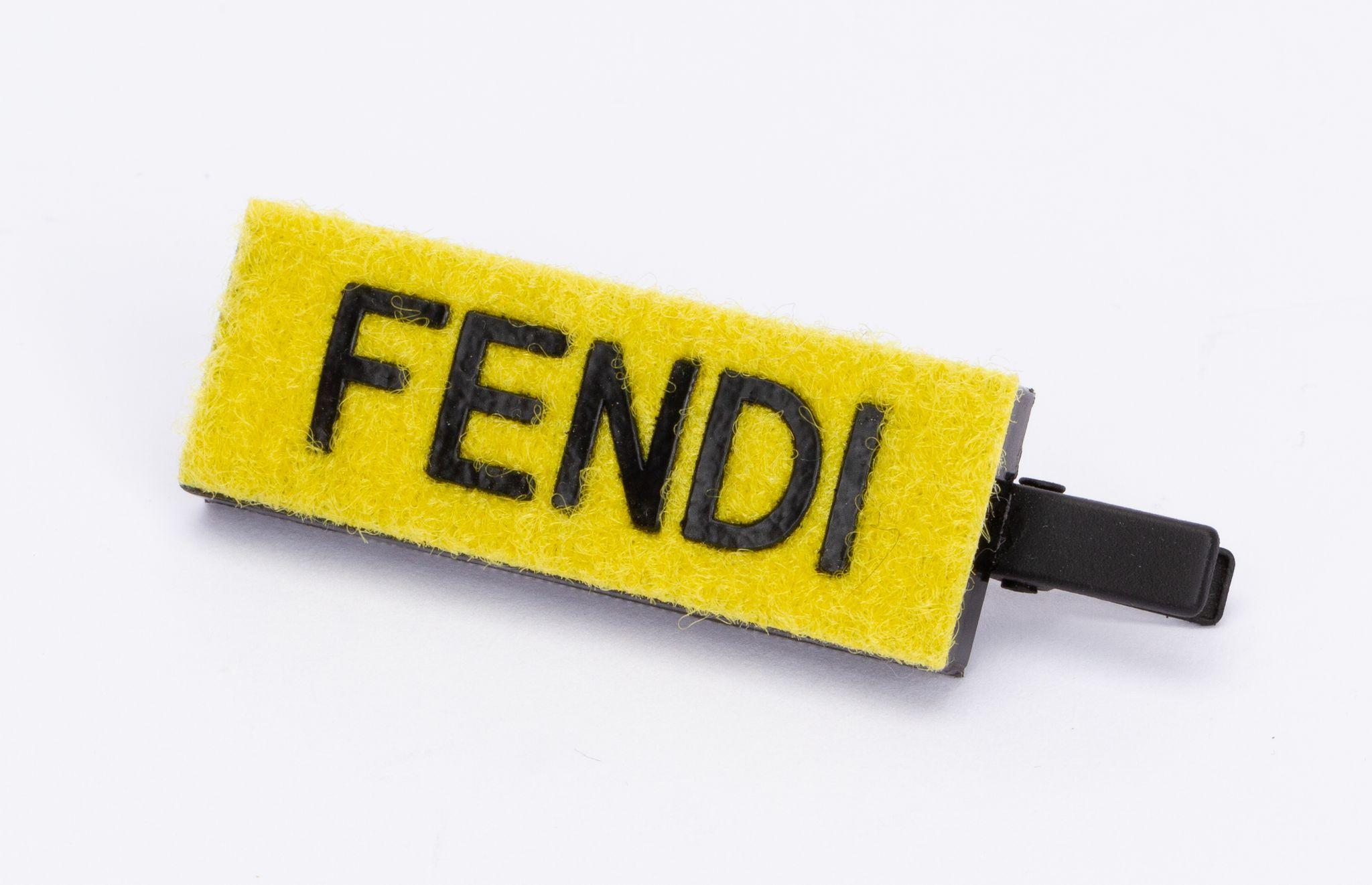 Fendi hairclip in yellow and black. It's rectangular and on the yellow fleece is Fendi written. The piece is new and includes the original box.