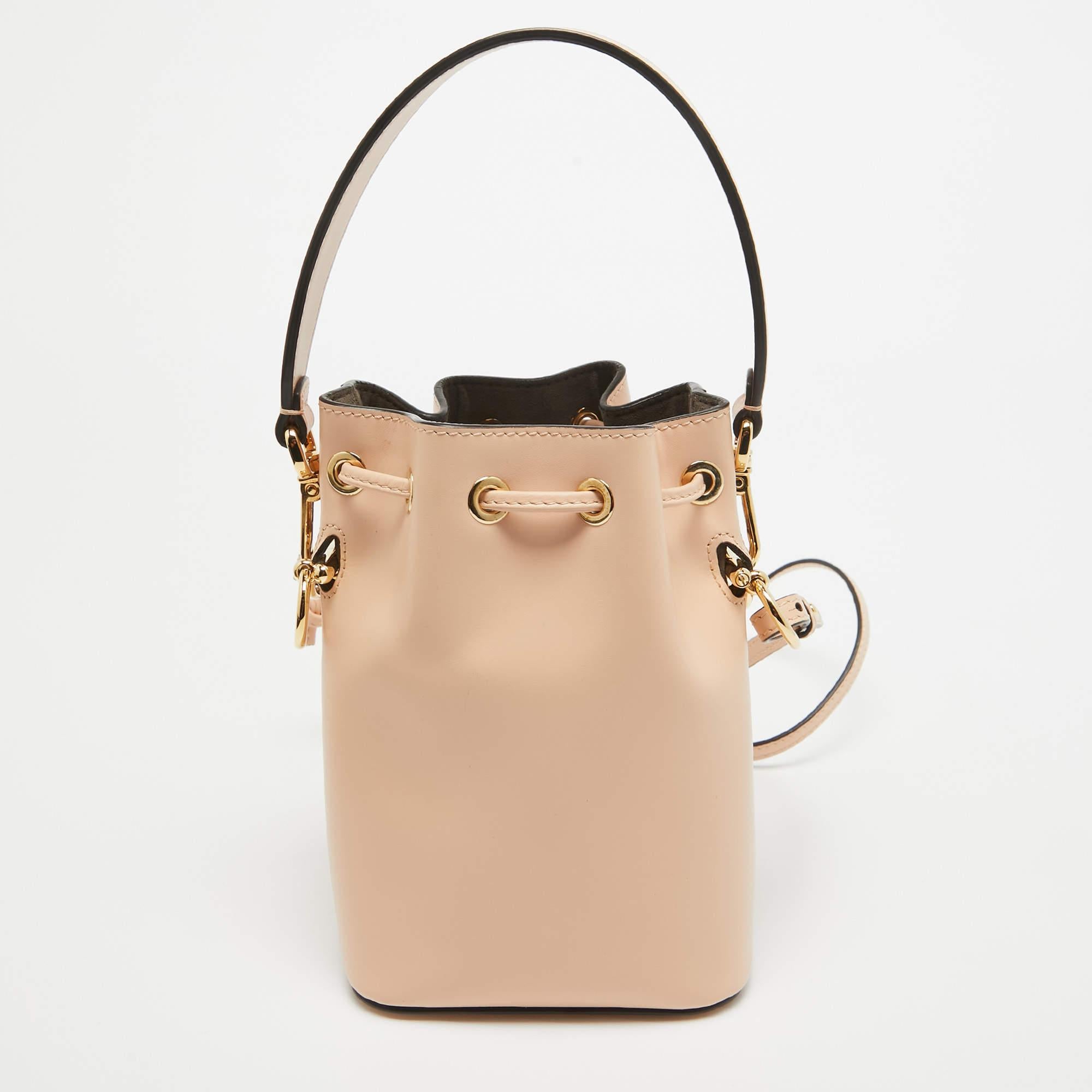 This wonderful Fendi design is made from leather and enhanced with gold-tone hardware. The bag has a bucket shape with a drawstring closure that secures the suede interior. It is complete with a single handle and a shoulder strap. Peach in color, it