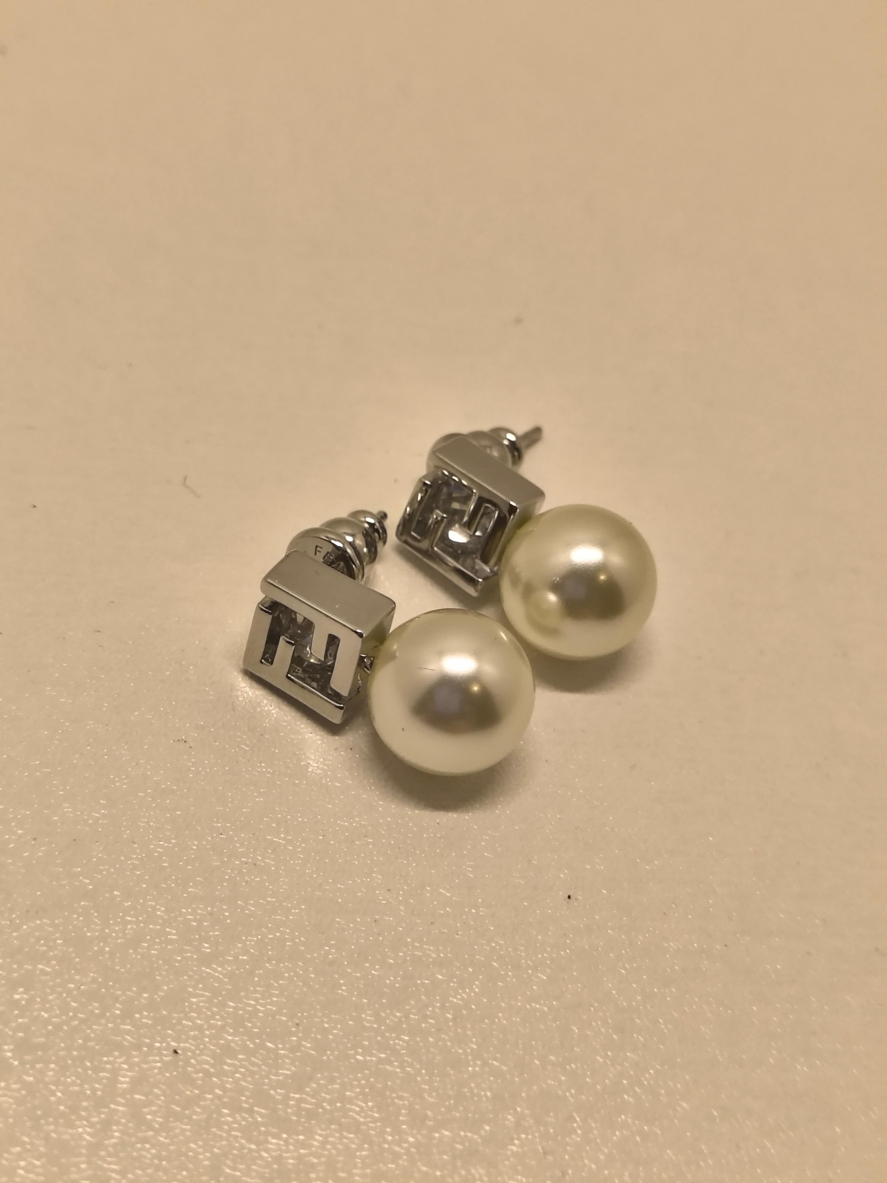 Questi orecchini con perle di Fendi catturano il caratteristico mix di lusso moderno ed eleganza senza tempo della maison. Caratterizzato da finte perle lucenti abbinate all'iconico logo FF in metallo argentato lucido, questo modello è una