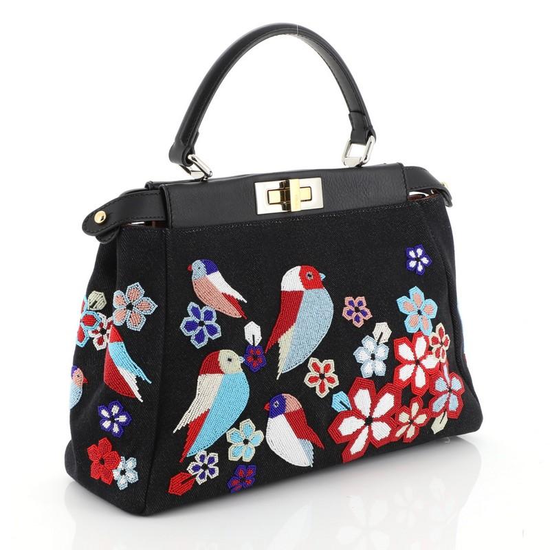This Fendi Peekaboo Bag Beaded Denim Regular, crafted from black beaded denim, features a top frame silhouette, flat leather handle, dual compartments with turn-lock and snap closures, and gold and silver-tone hardware. It opens to a pink leather