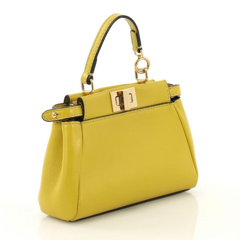 This Fendi Peekaboo Bag Leather Micro, crafted from yellow leather, features a top frame silhouette, flat leather handle, dual compartments with turn-lock and snap closures, and gold-tone hardware. It opens to a gray microfiber interior with side