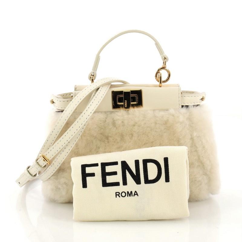 This Fendi Peekaboo Bag Shearling Micro, crafted from off white shearling, features a top frame silhouette, flat leather handle, dual compartments, and gold-tone hardware. Its turn-lock closure opens to a gray microfiber interior with side slip
