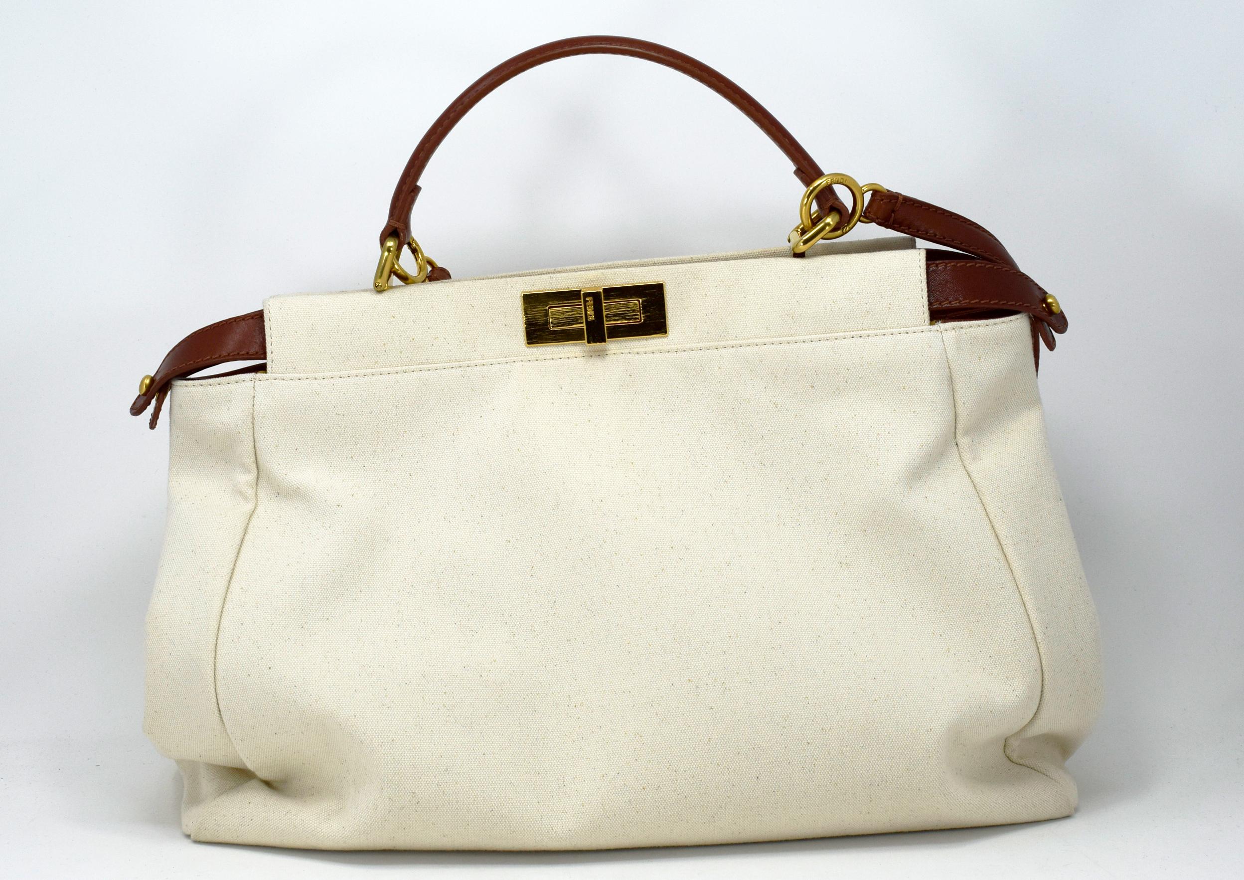 Fendi Peekaboo Handbag Canvas Large is one of Fendi best known designs exuding a luxurious yet minimalist appearance. Crafted in off white canvas, this versatile and stylish satchel features a flat brown leather top handle, protective base studs and
