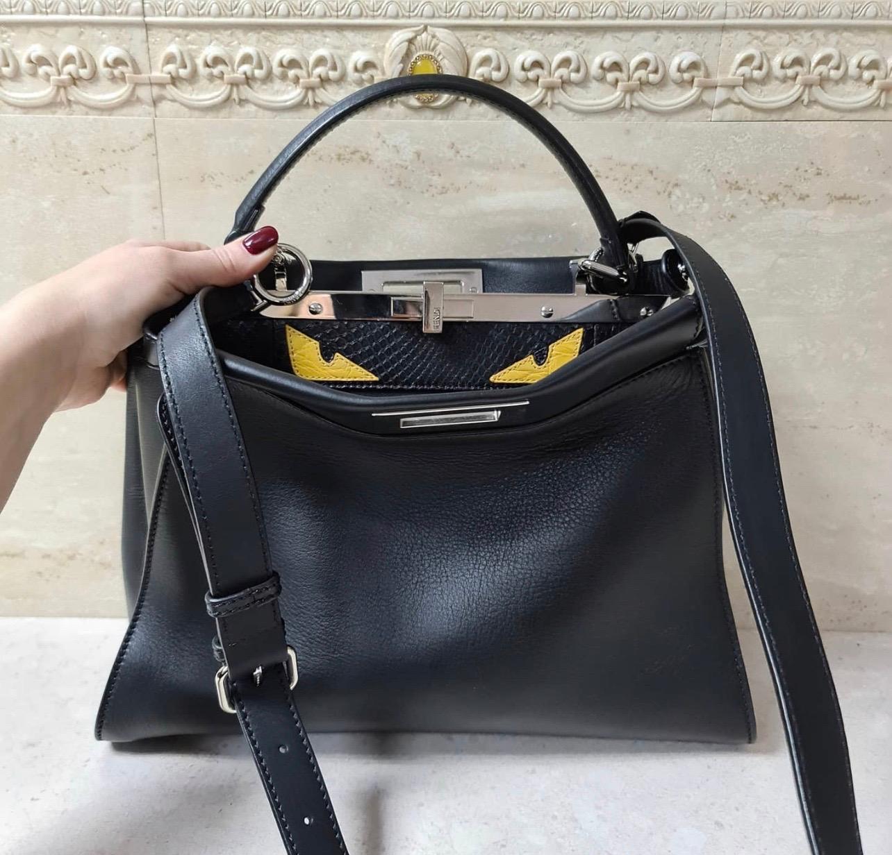 This Fendi Monster Peekaboo Bag Calfskin and Python Medium, crafted from black calfskin leather, features short leather top handle, protective base studs, framed top, and silver-tone hardware. 
Its double-sided turn-lock closures open to a genuine