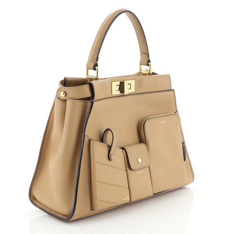 This Fendi Peekaboo Utility Bag Leather Regular, crafted from brown leather, features short leather top handle, exterior pockets, protective base studs, and gold-tone hardware. Its two compartments with turn-lock and zip closures open to a brown