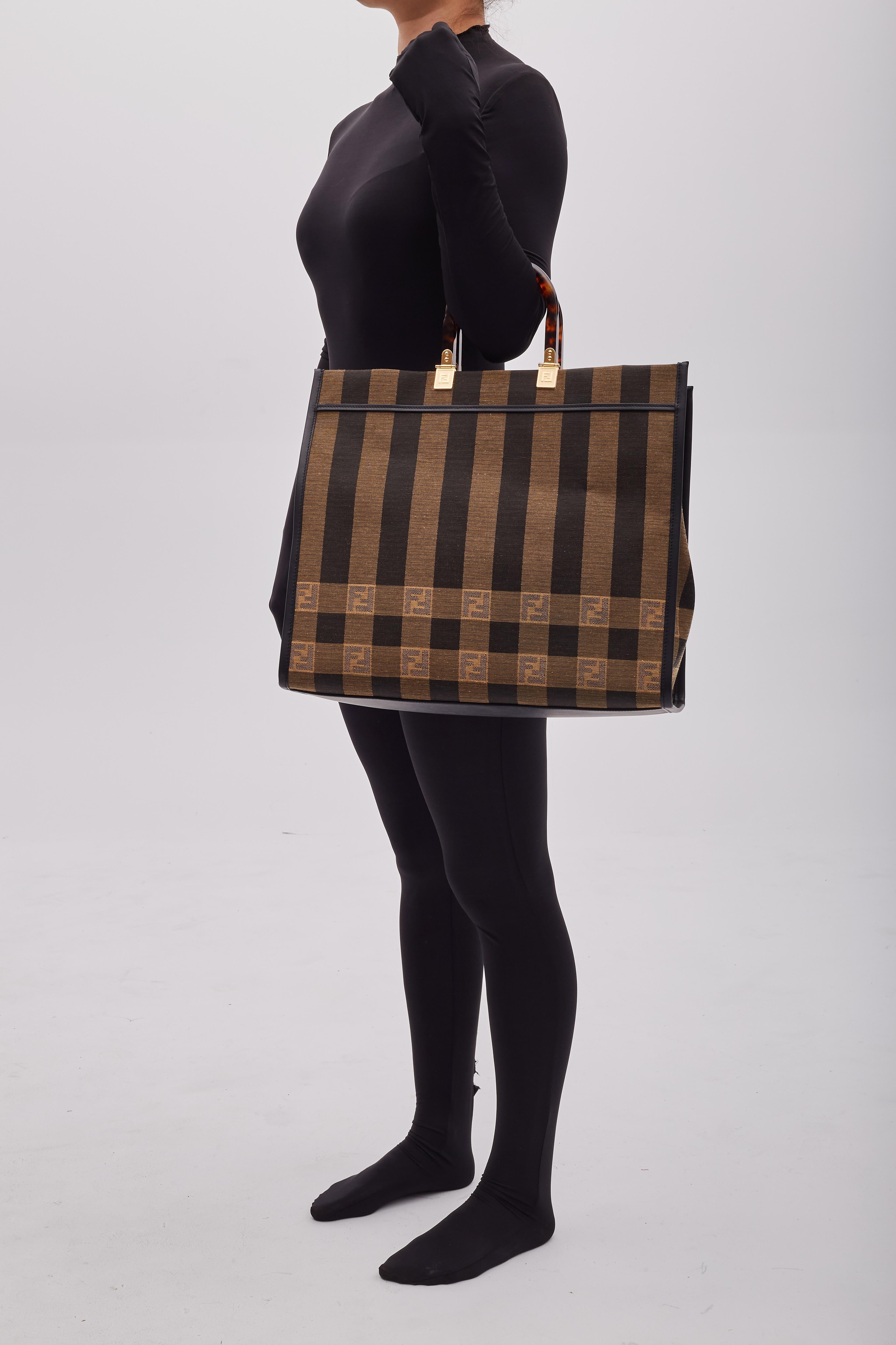 This Fendi shopping tote is made of gingham jacquard striped fabric with black leather trim. The bag features resin tortoiseshell top handles, gold hardware, an open top, and a spacious interior with a zipper pocket.

Color: Tobacco black /