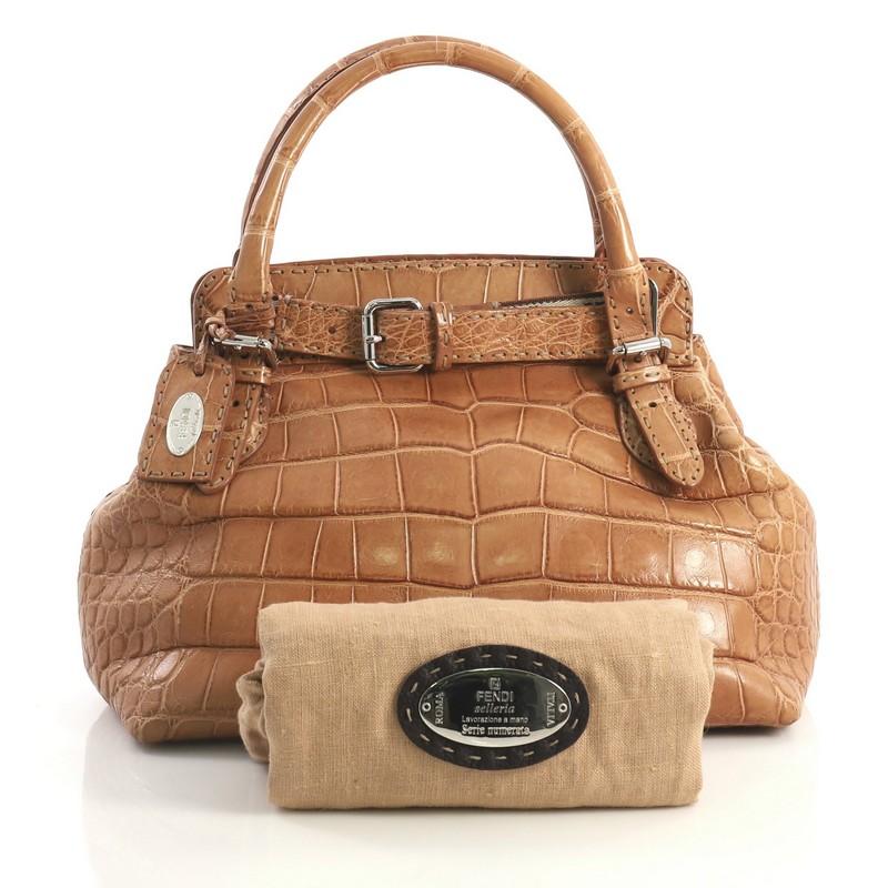 This Fendi Selleria Villa Borghese Tote Alligator Small, crafted in genuine brown alligator, features dual rolled handles, buckle details and silver-tone hardware. Its belted closure opens to a brown fabric interior with side zip pocket. 

Estimated