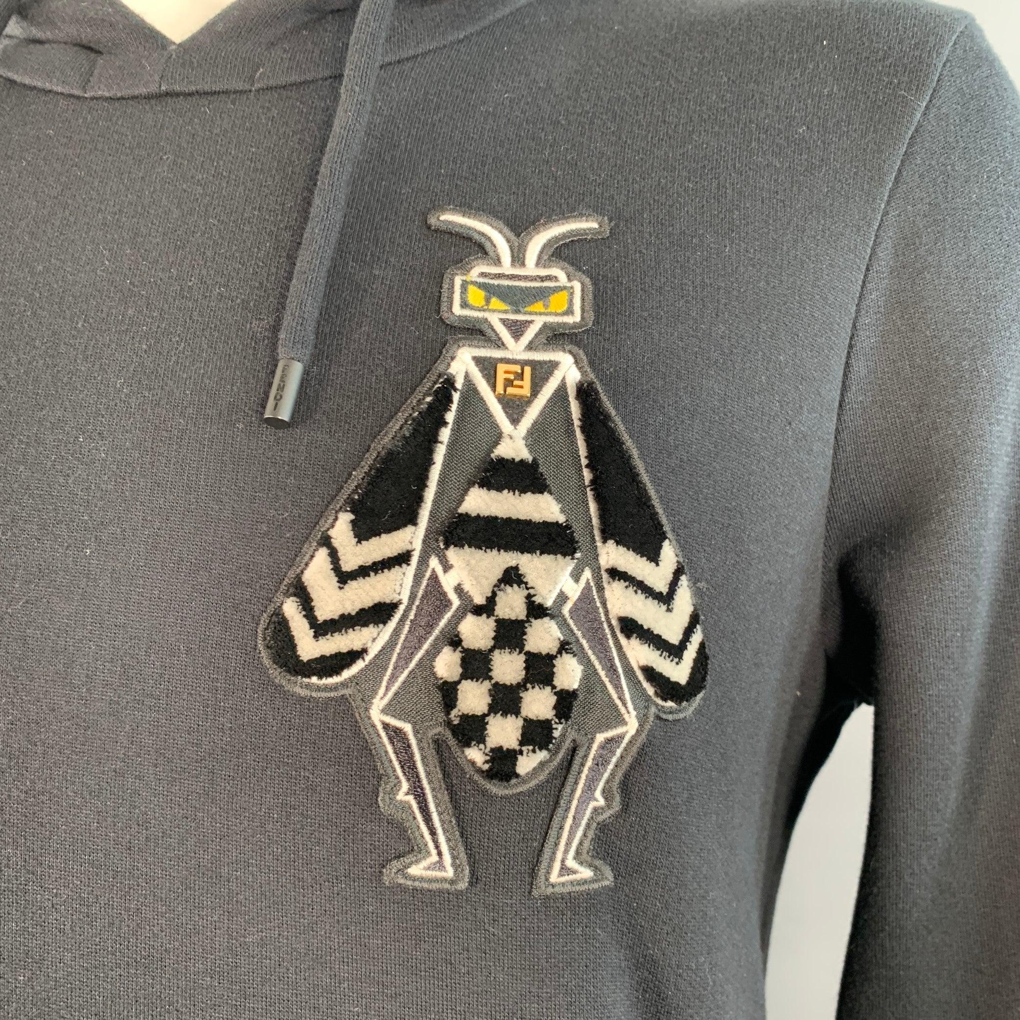 Felpa Fendi
in cotone nero con cappuccio, due applicazioni di insetti astratti e due tasche a filetto. Made in Italy. Eccellente condizione di usato. 

Contrassegnato:   taglia non segnata, etichetta del tessuto rimossa. 

Misure: 
 
Spalla: 19,5