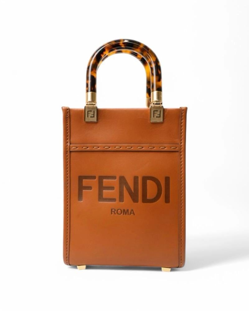 Sac signé Fendi, modèle Sunshine en taille mini, en cuir lisse de couleur biscuit avec des ferrures dorées. Dépourvu de fermoir, doublé intérieurement de toile, le sac est spacieux et permet d'emporter l'essentiel. Équipé d'une double poignée en  en